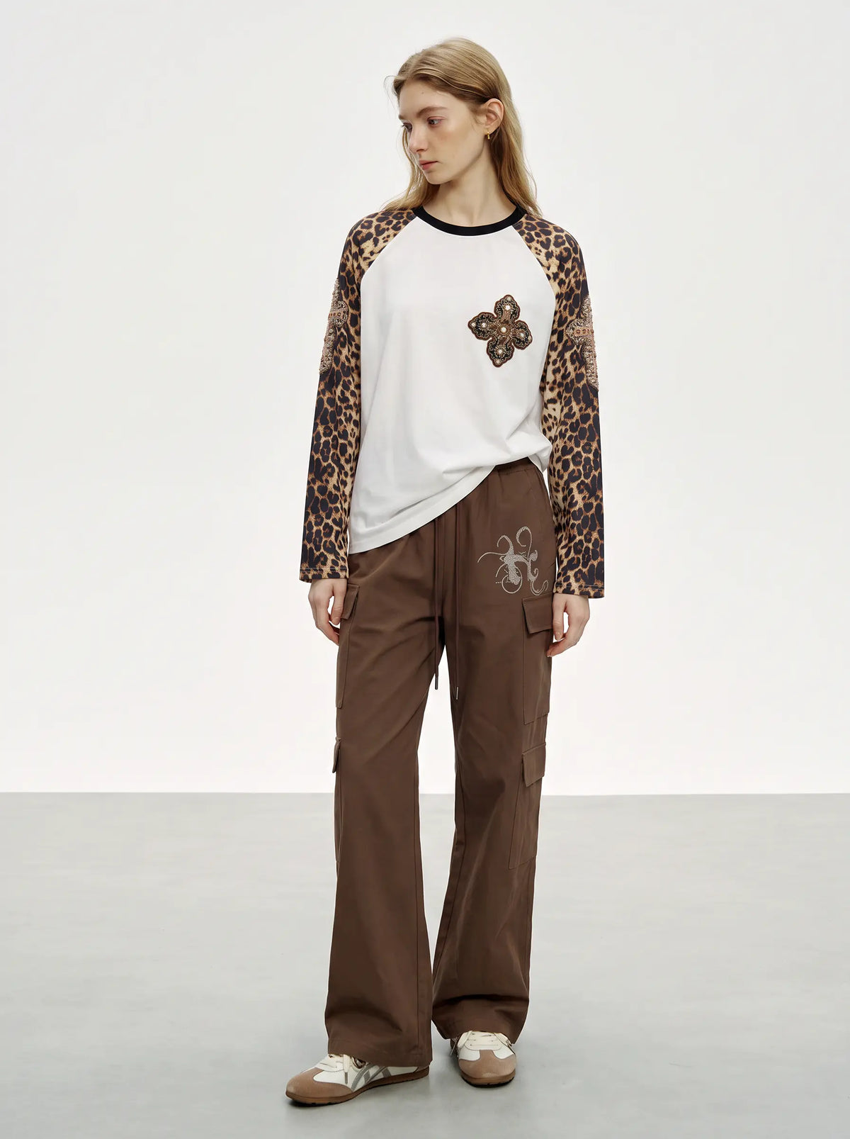 A model stands in a studio wearing a white raglan T-shirt with leopard-print sleeves, brown wide-leg cargo pants, and brown slip-on shoes. TCH Leopard Print Sleeve Embellished Cross Raglan Long Sleeve T-Shirt