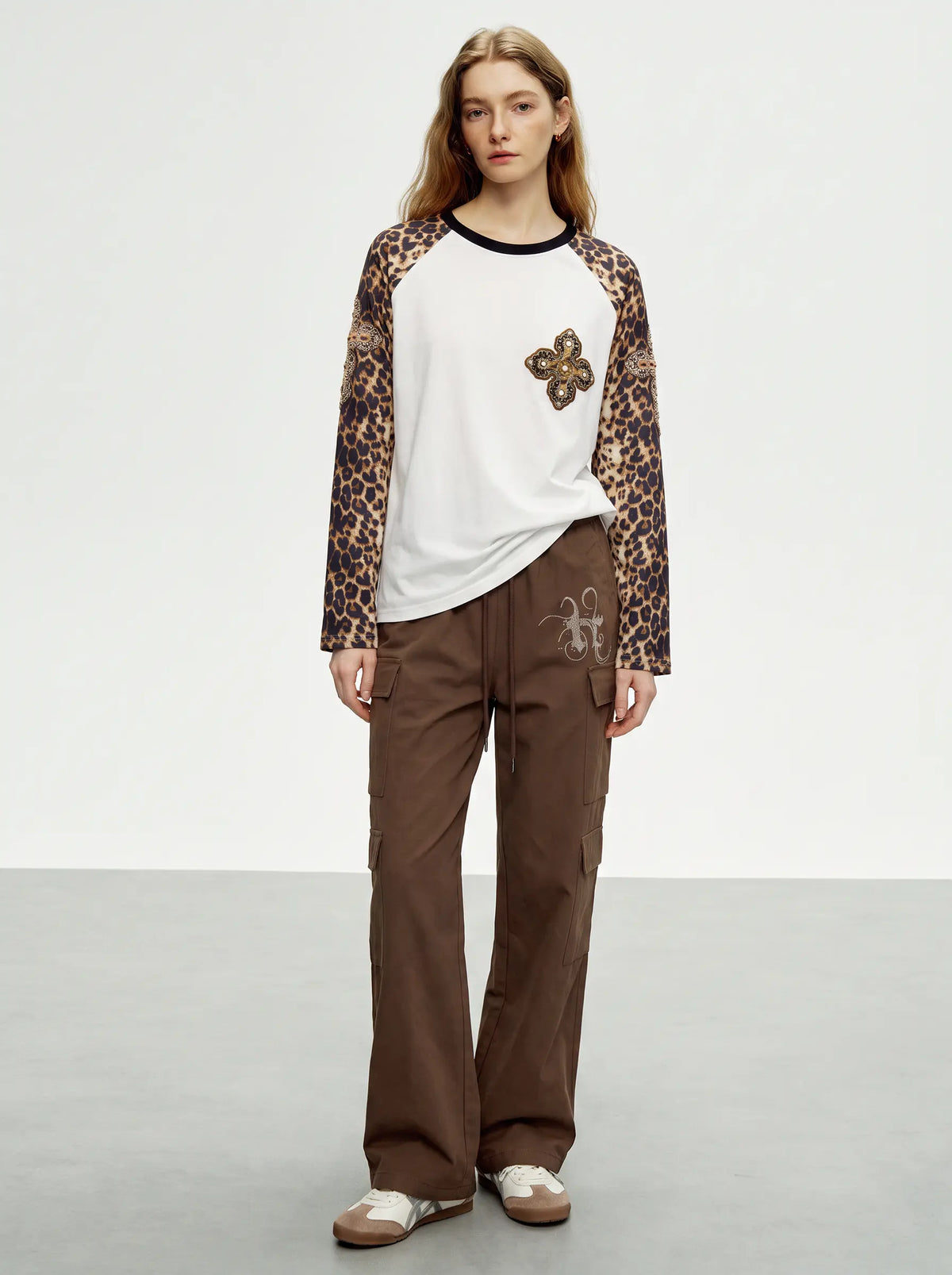 A model stands in a studio wearing a white raglan long-sleeve shirt with leopard-print sleeves, a butterfly applique on the chest, brown cargo pants, and brown slip-on shoes. TCH Leopard Print Sleeve Embellished Cross Raglan Long Sleeve T-Shirt