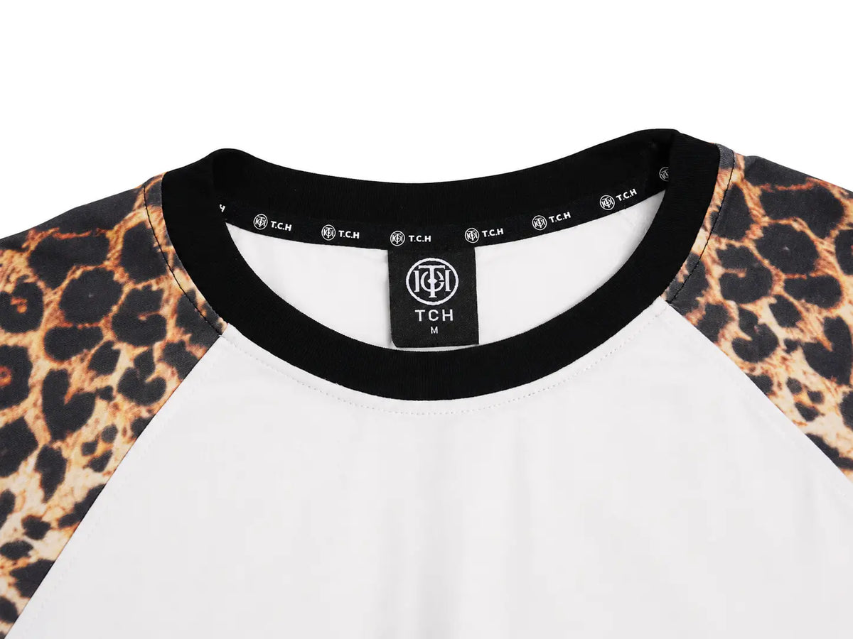 Close-up of a raglan baseball t-shirt by TCH, featuring a white body, black ribbed collar, and leopard print sleeves on a white background. TCH Leopard Print Sleeve Embellished Cross Raglan Long Sleeve T-Shirt