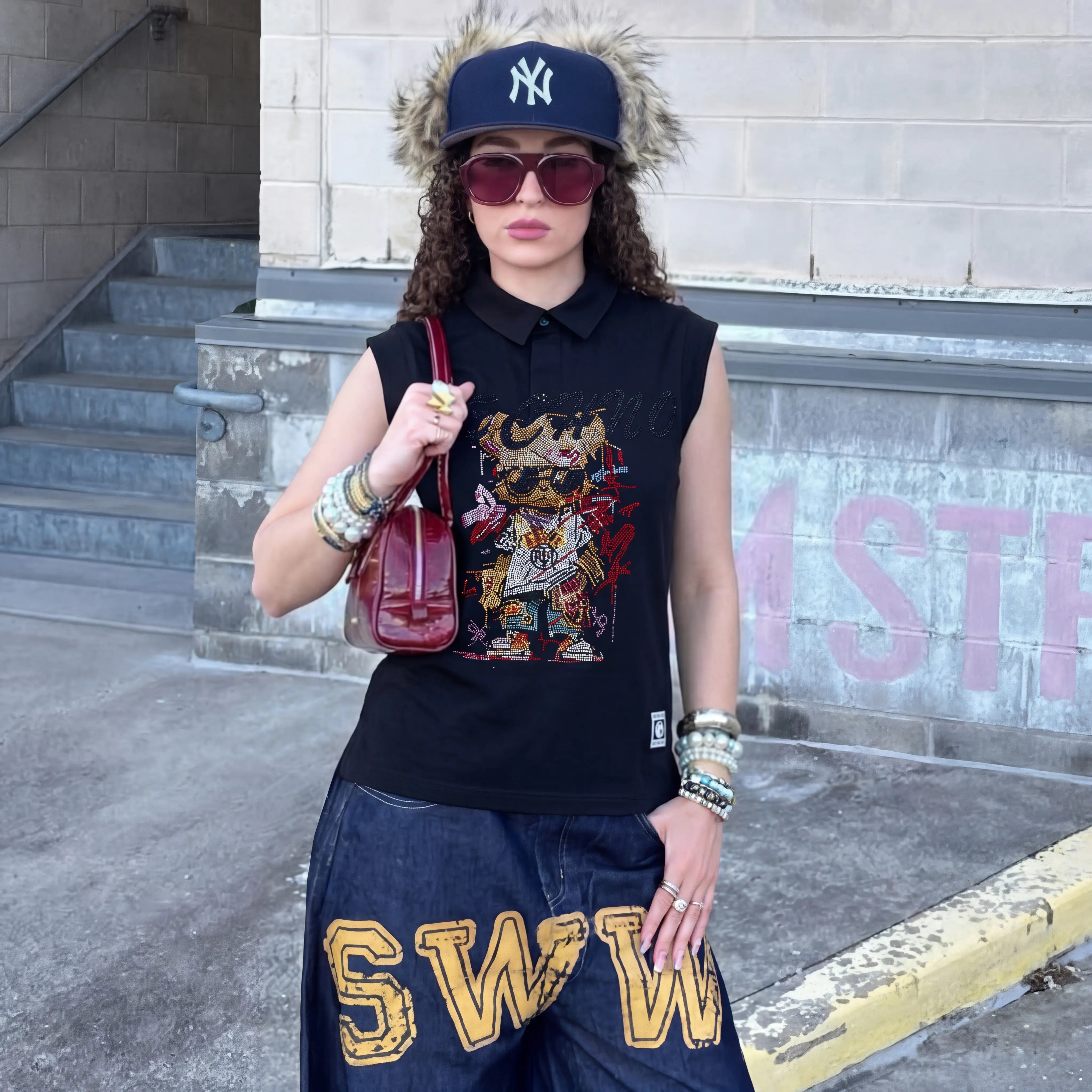 Person wearing a black sleeveless shirt with a colorful graphic, blue cap, sunglasses, and blue pants with yellow text, standing on a street. TCH Leopard Rhinestone Sleeveless Polo Shirt