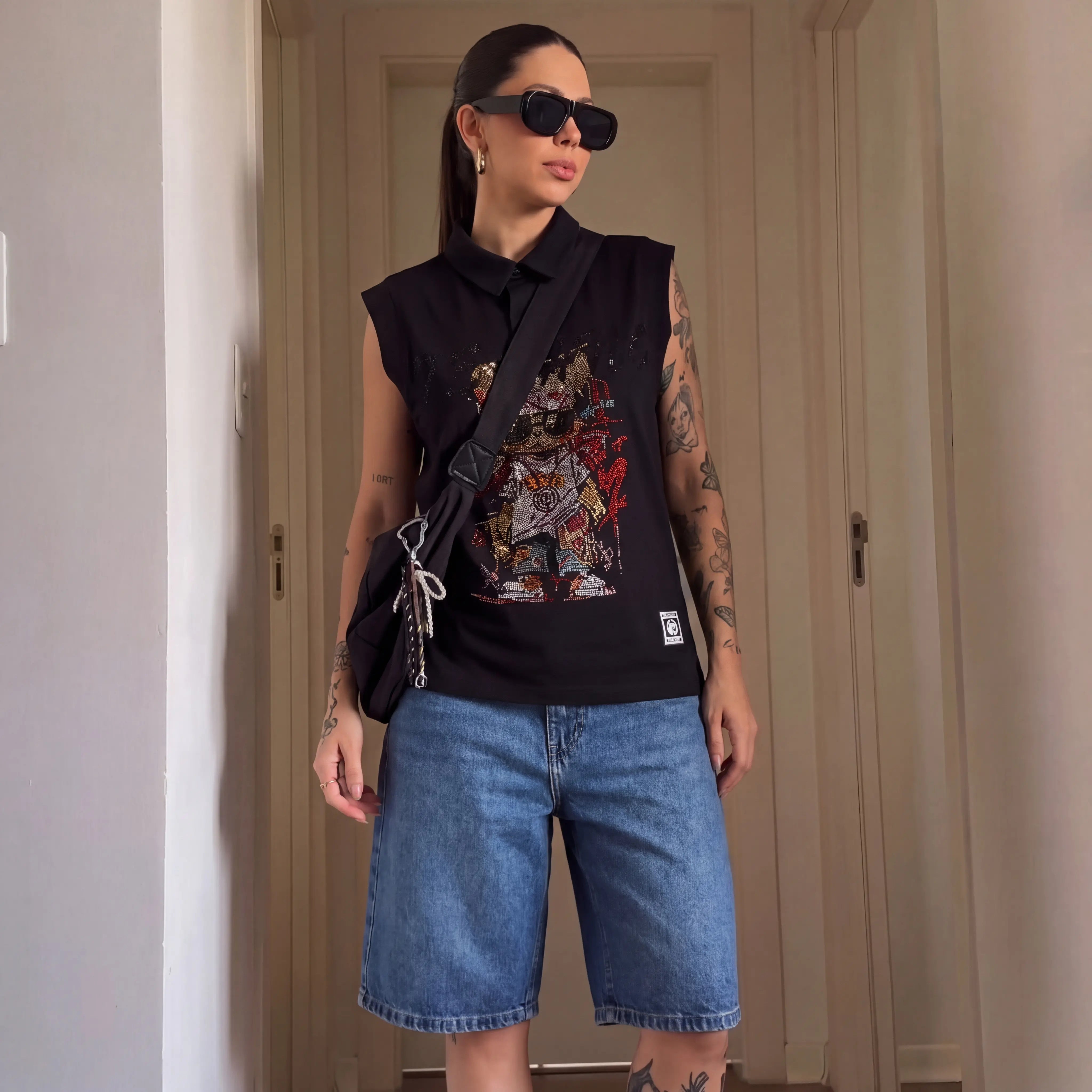 Person wearing a black sleeveless shirt with colorful graphics and blue shorts, standing indoors. TCH Leopard Rhinestone Sleeveless Polo Shirt