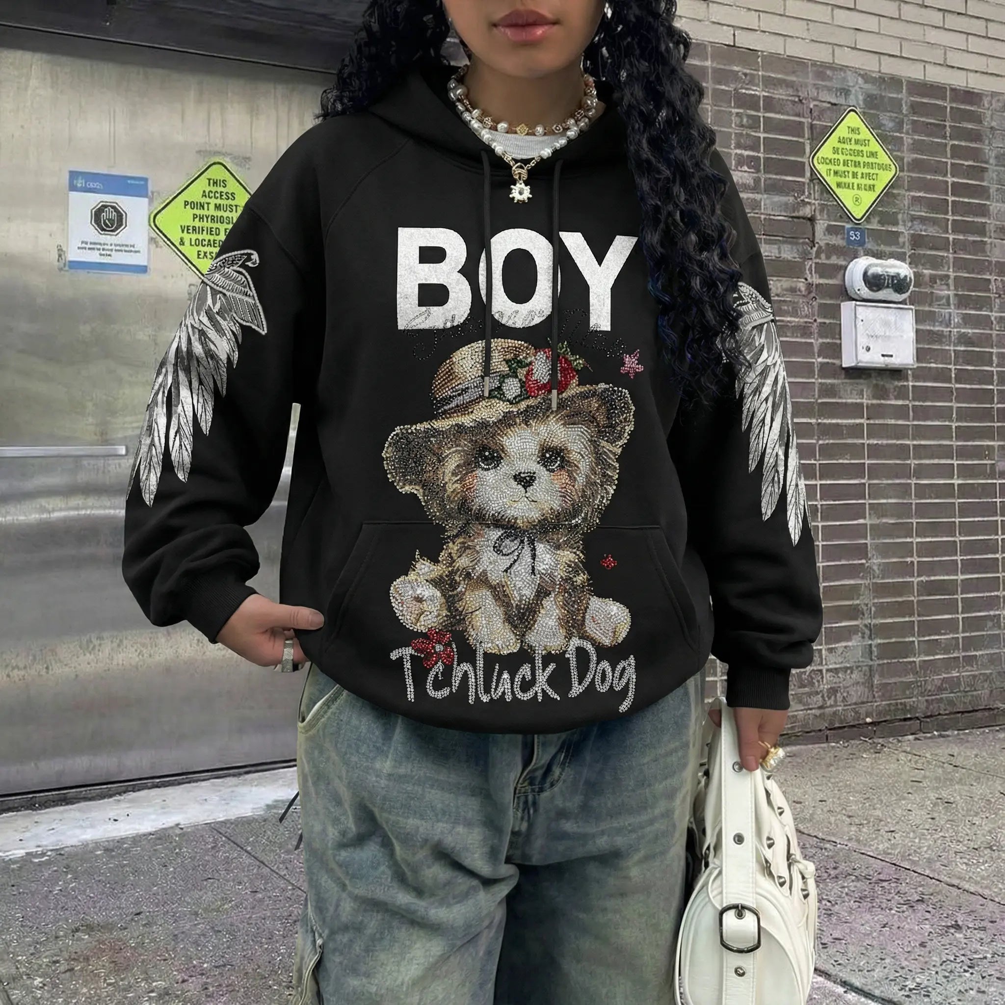 Person wearing a black hoodie with a teddy bear graphic and text, standing against a brick wall. TCH Luck Dog Rhinestone Hooded Sweatshirt-