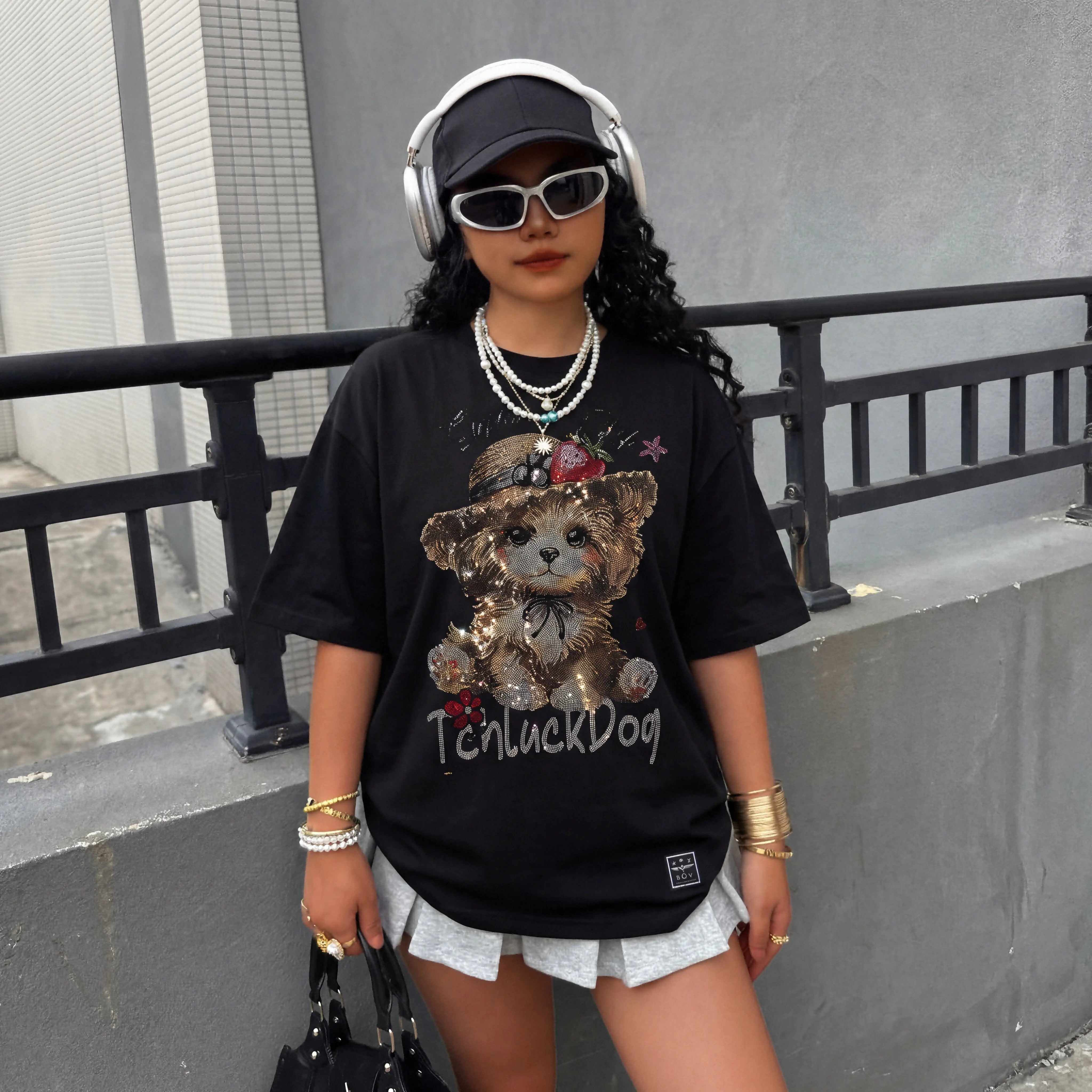 Person wearing a black t-shirt with a teddy bear graphic and text, standing against a gray wall. TCH Luck Dog Rhinestone T-Shirt