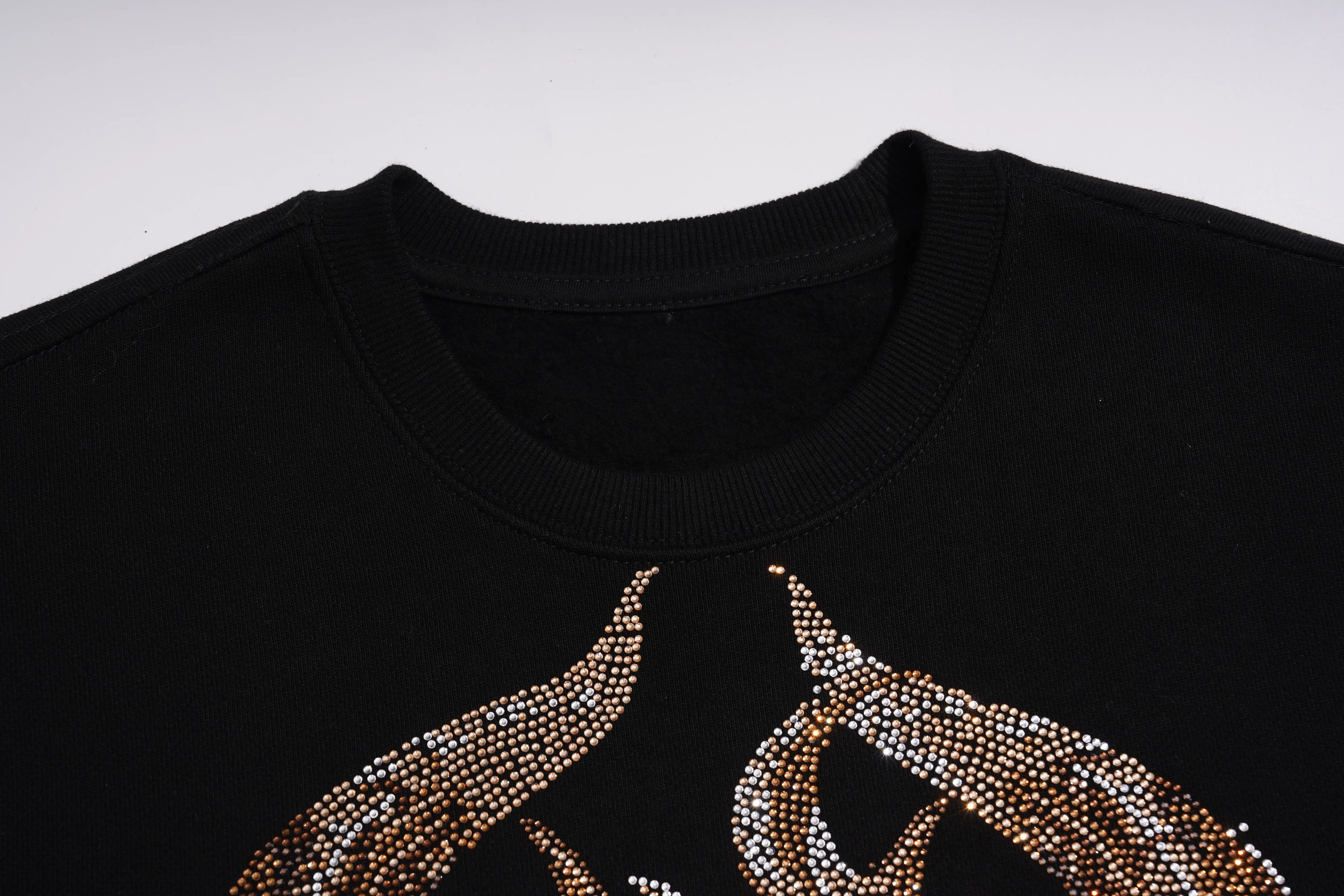 Close-up of a black crewneck sweatshirt featuring a large graphic design on the front made of gold and silver rhinestones. TCH Luxury Gold Dragon Rhinestone Graphic Black Sweatshirt