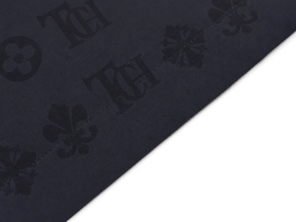 A close-up of a dark navy fabric with an embossed repeating pattern of clovers and monogrammed letters, shown diagonally against a white background. TCH Luxury Monogram Hooded Windbreaker Jacket