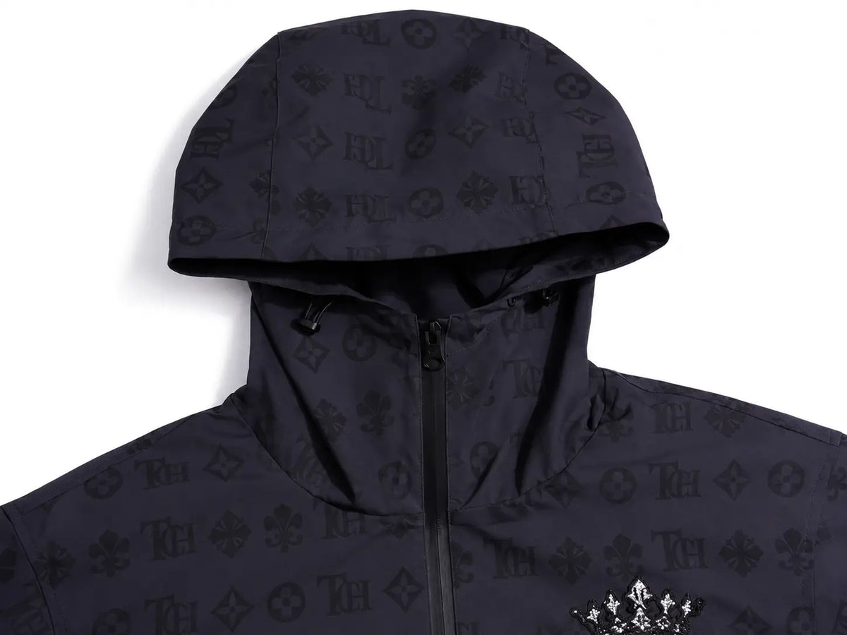 A close-up of a black hooded jacket featuring an all-over tonal Louis Vuitton monogram pattern, with a black zipper and a small silver graphic on the chest, set against a plain white background. TCH Luxury Monogram Hooded Windbreaker Jacket