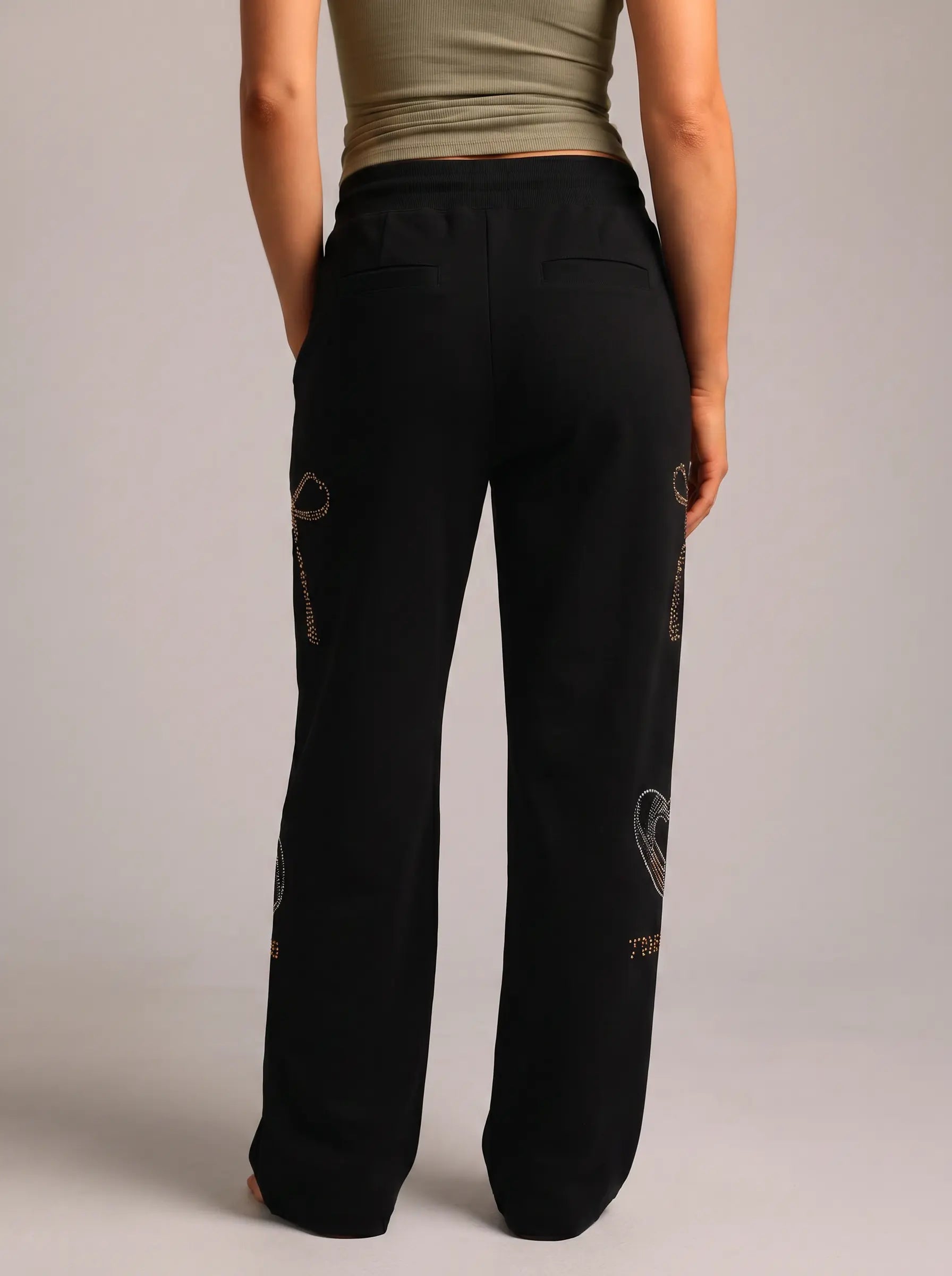 Black wide-leg sweatpants with gold chain and heart embroidery, shown from the back on a model wearing an olive green top against a light gray studio background. TCH Luxury Rhinestone High Heel Graphic Black Sweatpants