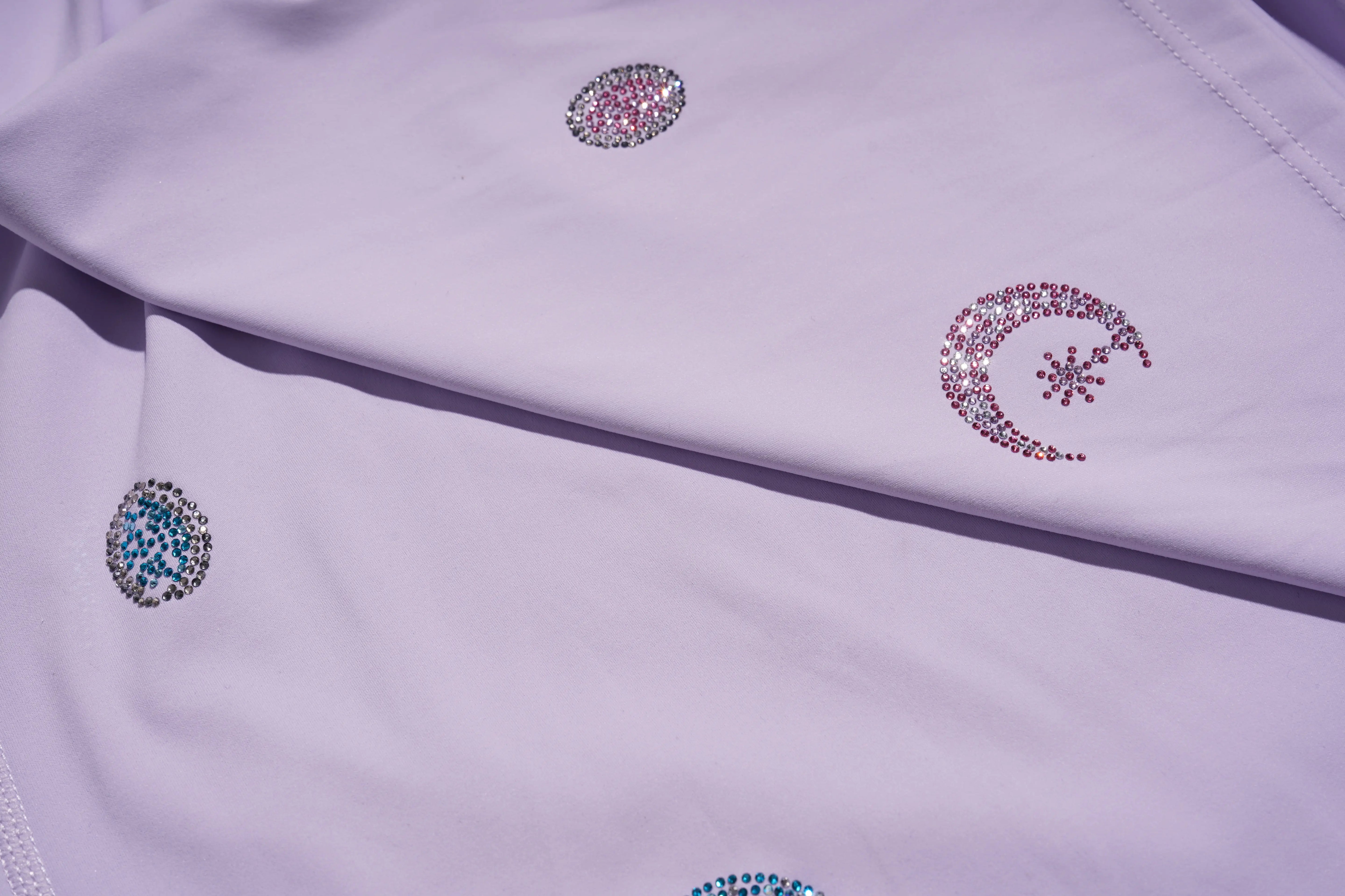 Close-up of a light purple garment with decorative gemstones on a matching fabric background. TCH Moonlight Rhinestone Wide-Leg Pants