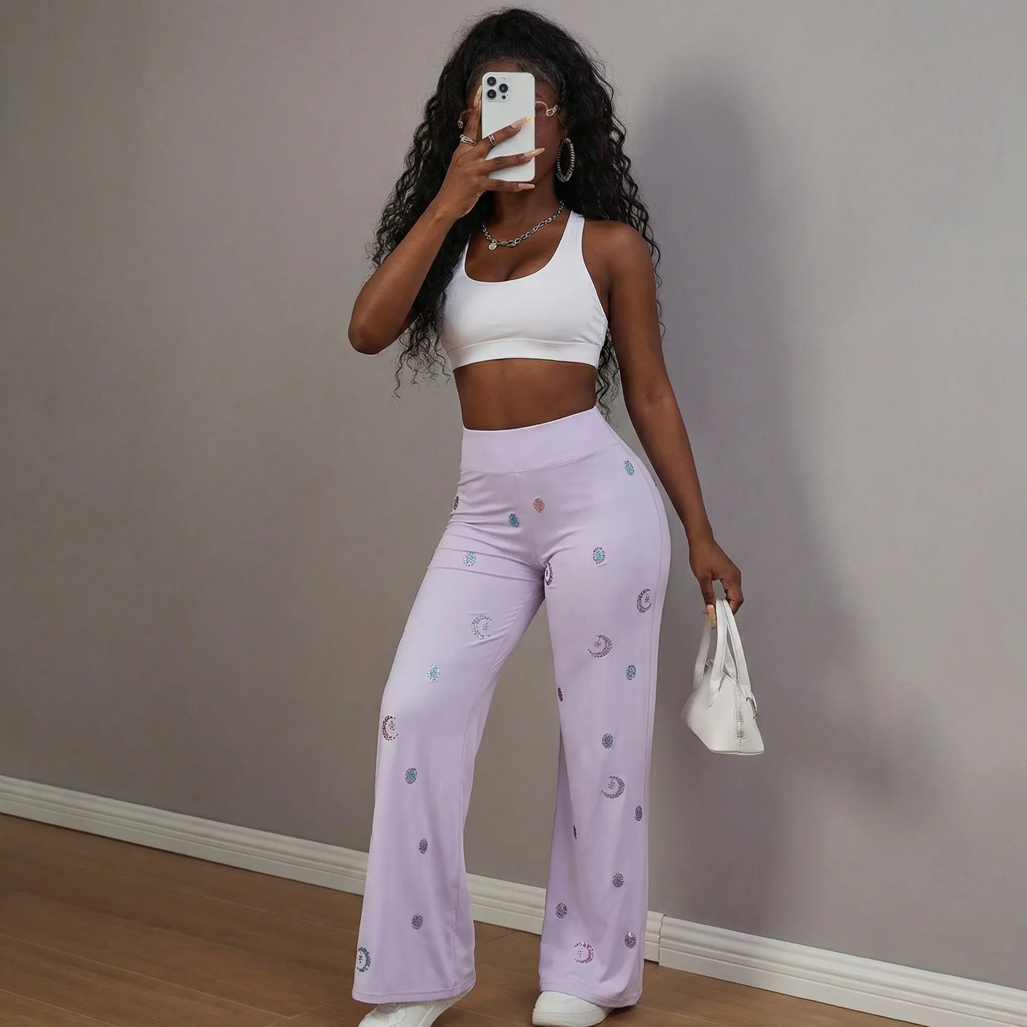 Woman wearing a white crop top and light purple pants with a pattern, holding a phone and a small bag against a plain wall. TCH Moonlight Rhinestone Wide-Leg Pants