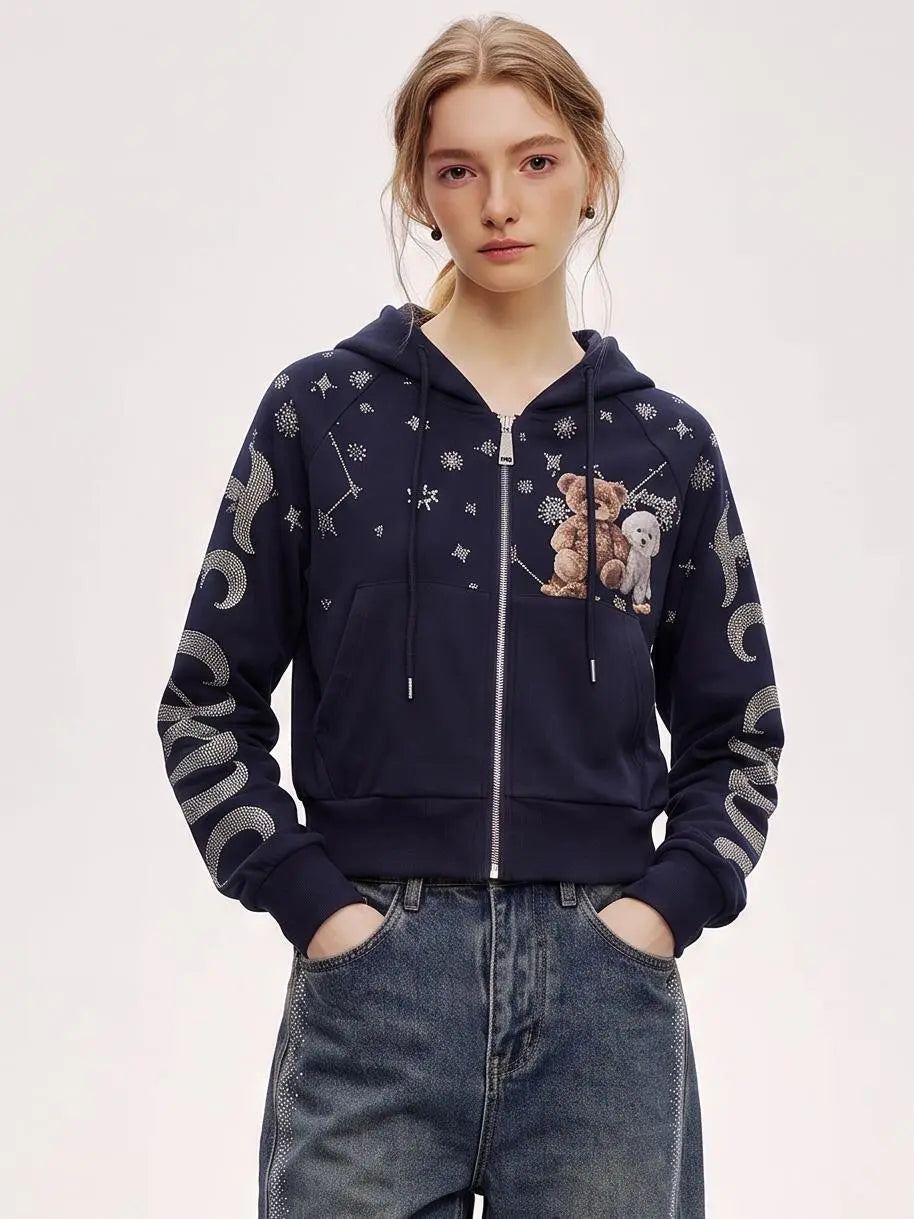 A model wearing a navy blue zip-up hoodie with teddy bear graphics and silver moon/sun prints on the sleeves, paired with blue jeans, against a plain light background. TCH Navy Teddy Bear Rhinestone Zip Hoodie