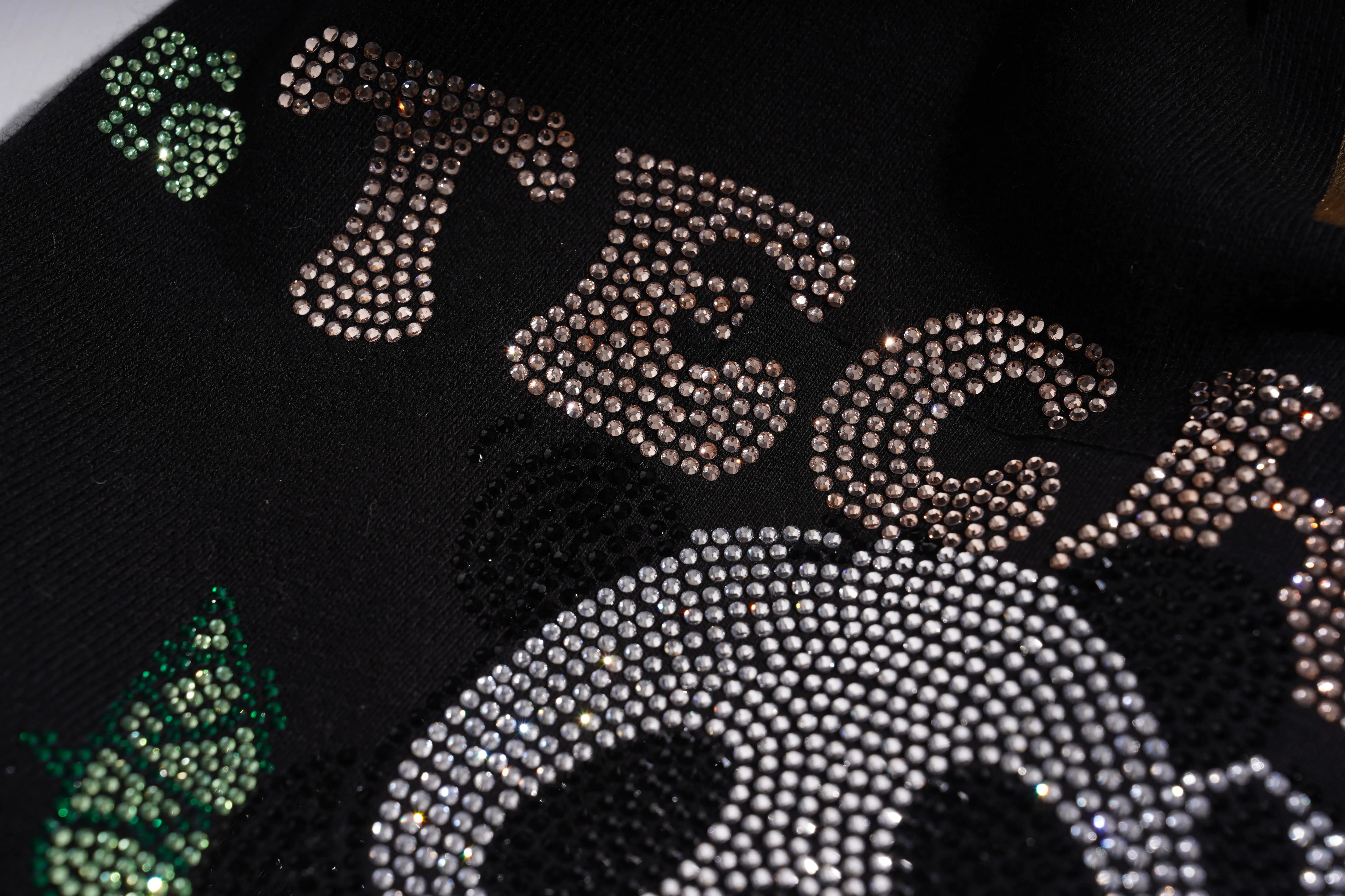 Close-up of a black surface with decorative text and patterns in various colors. TCH Panda Rhinestone Black Jogger Pants
