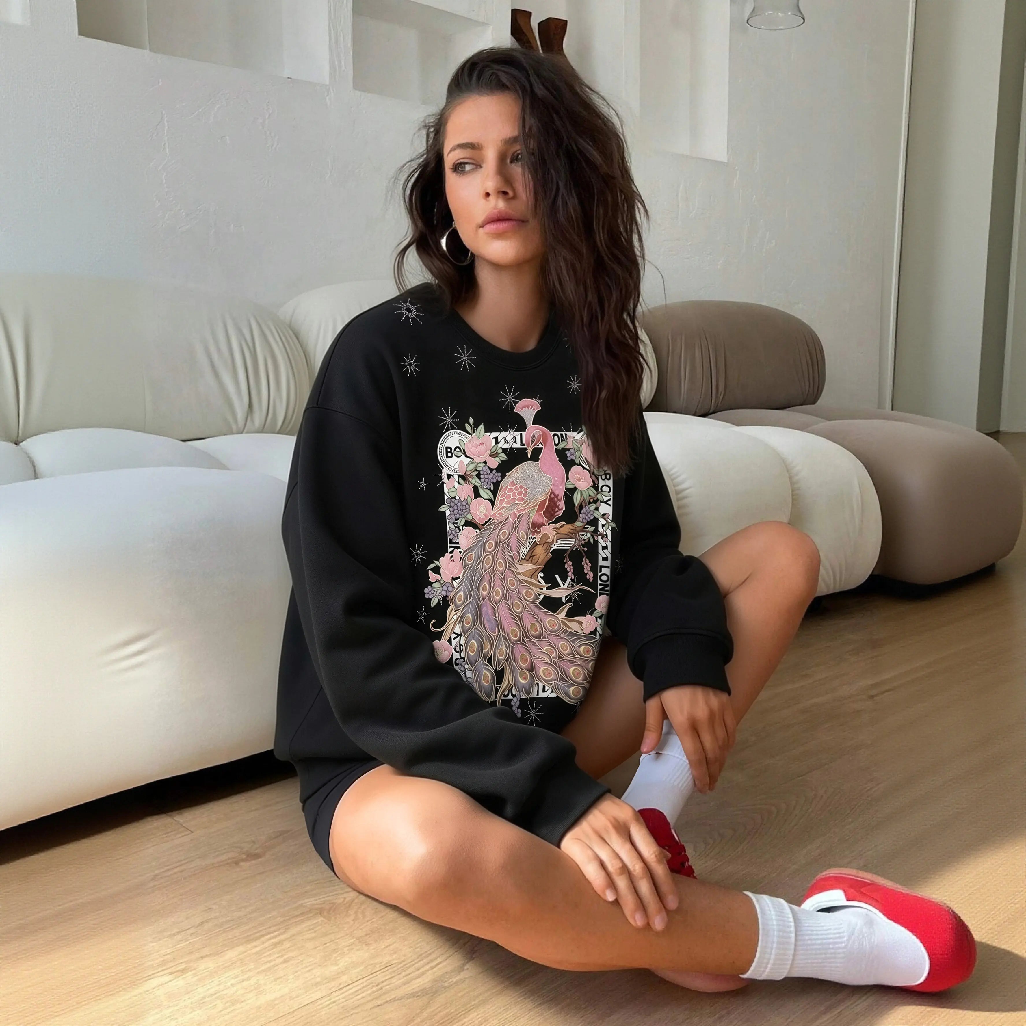 Woman sitting on the floor wearing a black sweatshirt with a peacock design in a living room. TCH Peacock Embroidered Rhinestone Sweatshirt
