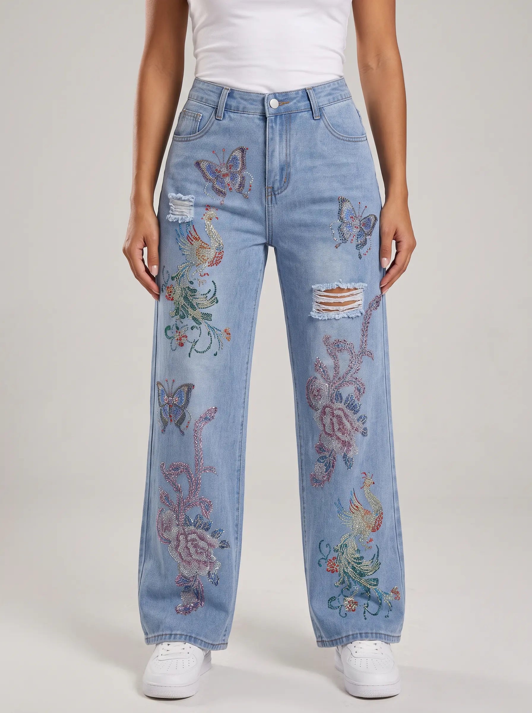 A model wearing light blue wide-leg denim jeans with colorful butterfly and floral embroidery, a white top, and white sneakers against a light gray studio background. TCH Phoenix & Butterfly Rhinestone Wide Leg Jeans