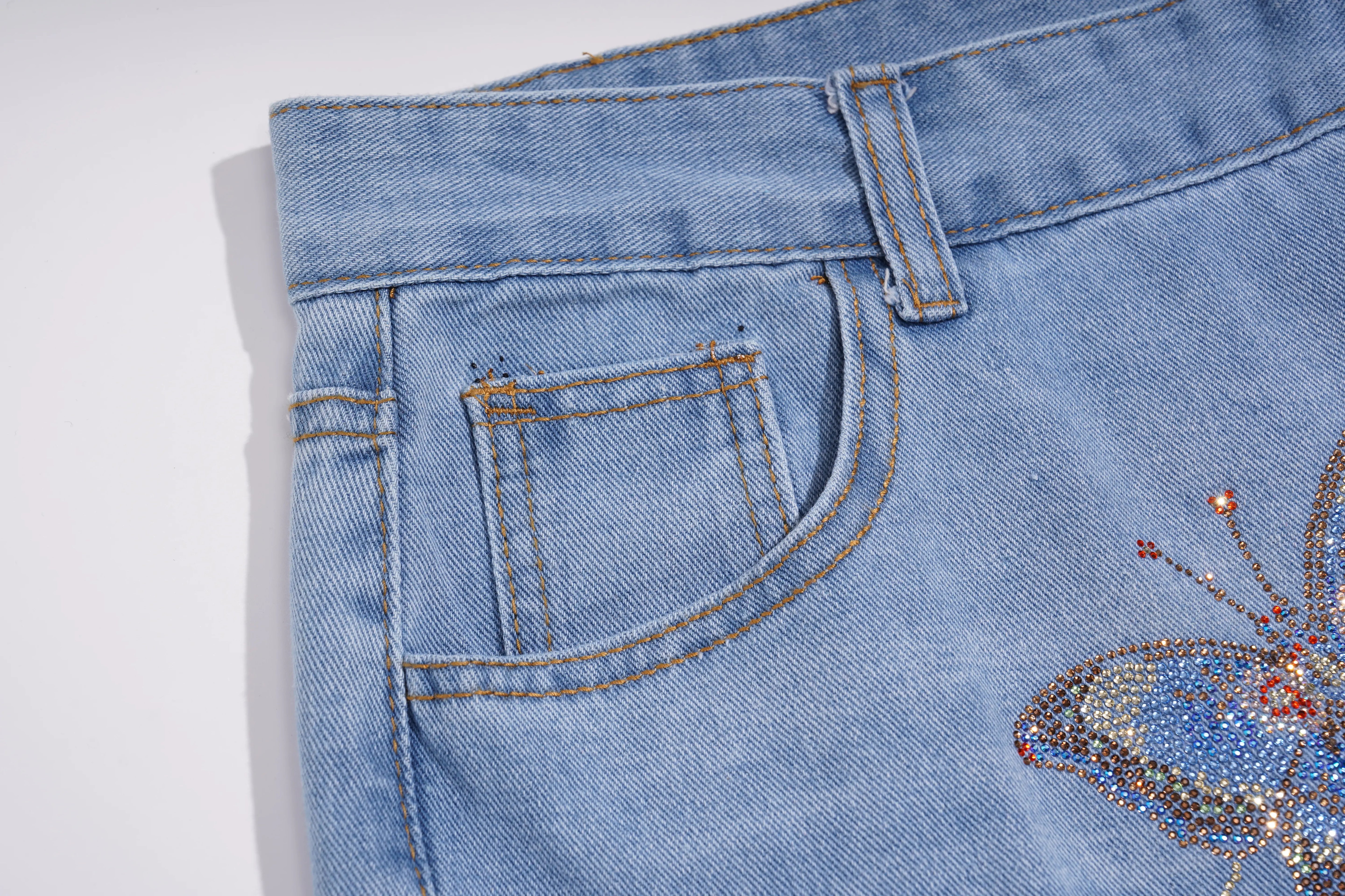 Close-up of light blue denim jeans showing the back pocket, belt loop, and a rhinestone-embellished butterfly detail on the leg. TCH Phoenix & Butterfly Rhinestone Wide Leg Jeans