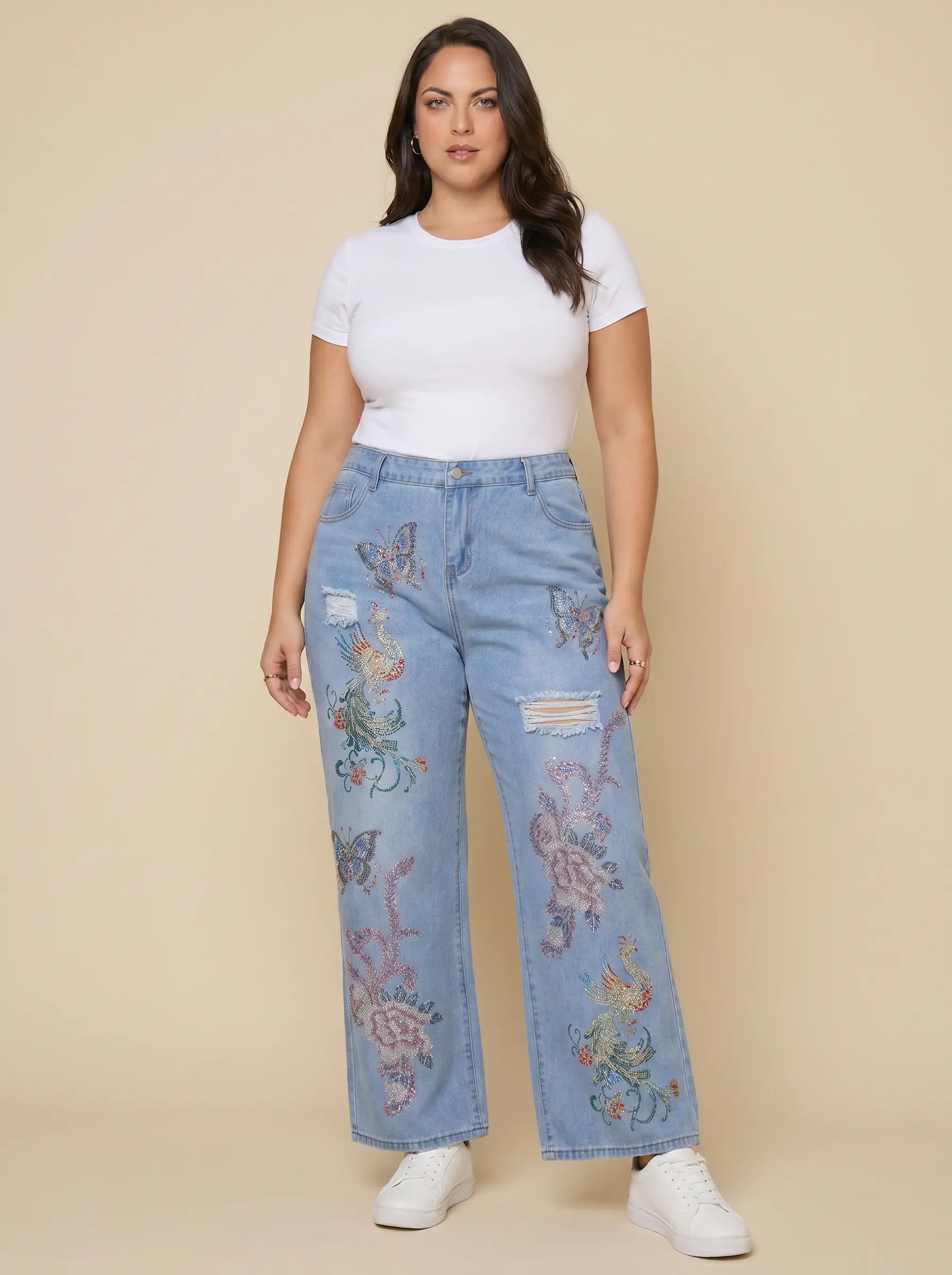 A woman modeling a pair of light-wash blue jeans with colorful butterfly and floral embroidery, styled with a white t-shirt and white sneakers against a solid beige background. TCH Phoenix & Butterfly Rhinestone Wide Leg Jeans