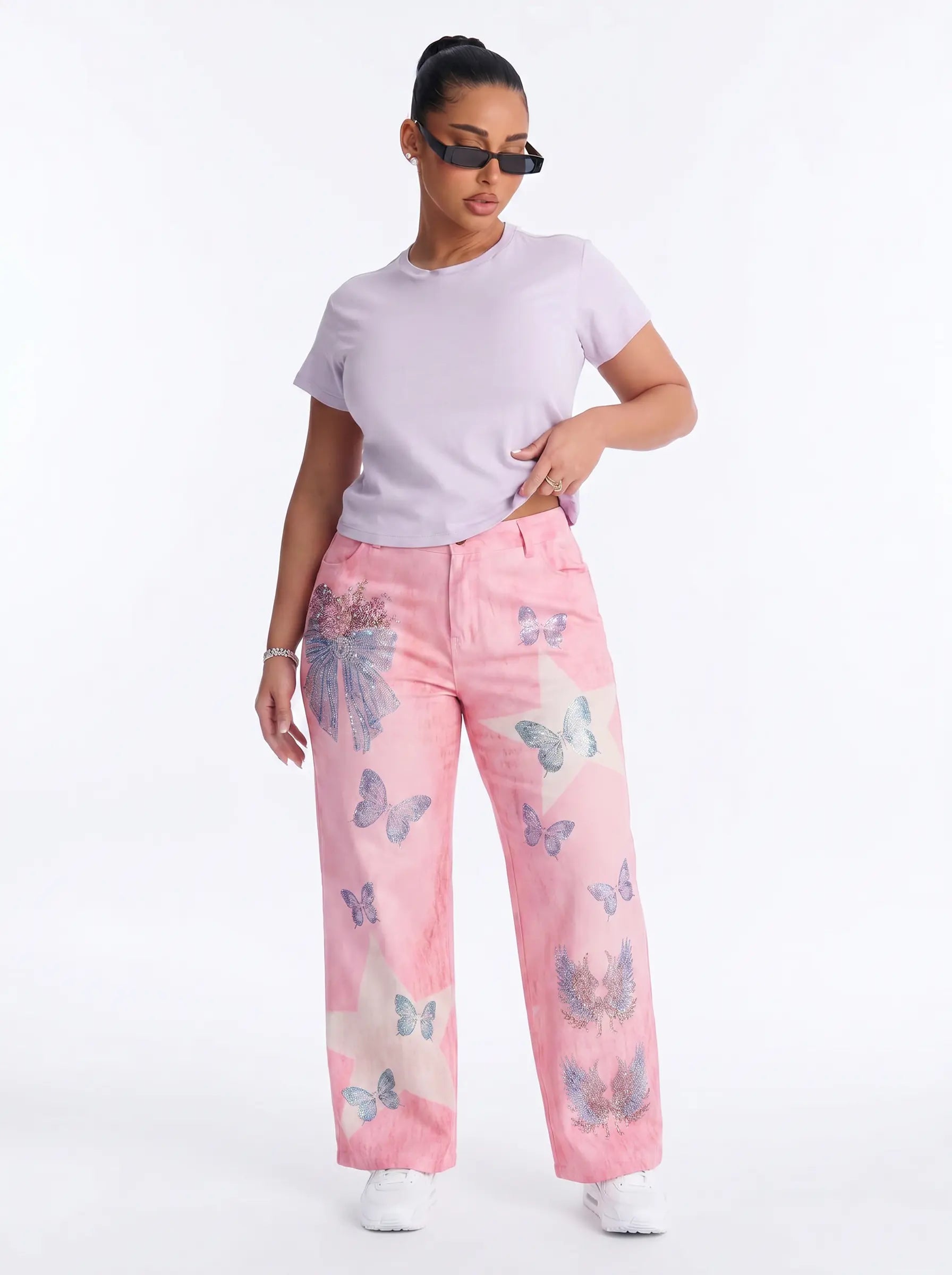 A model wearing pink wide-leg jeans with a butterfly print, styled with a light purple t-shirt and sunglasses against a white studio background. TCH Pink Butterfly Rhinestone Star Wide Leg Jeans