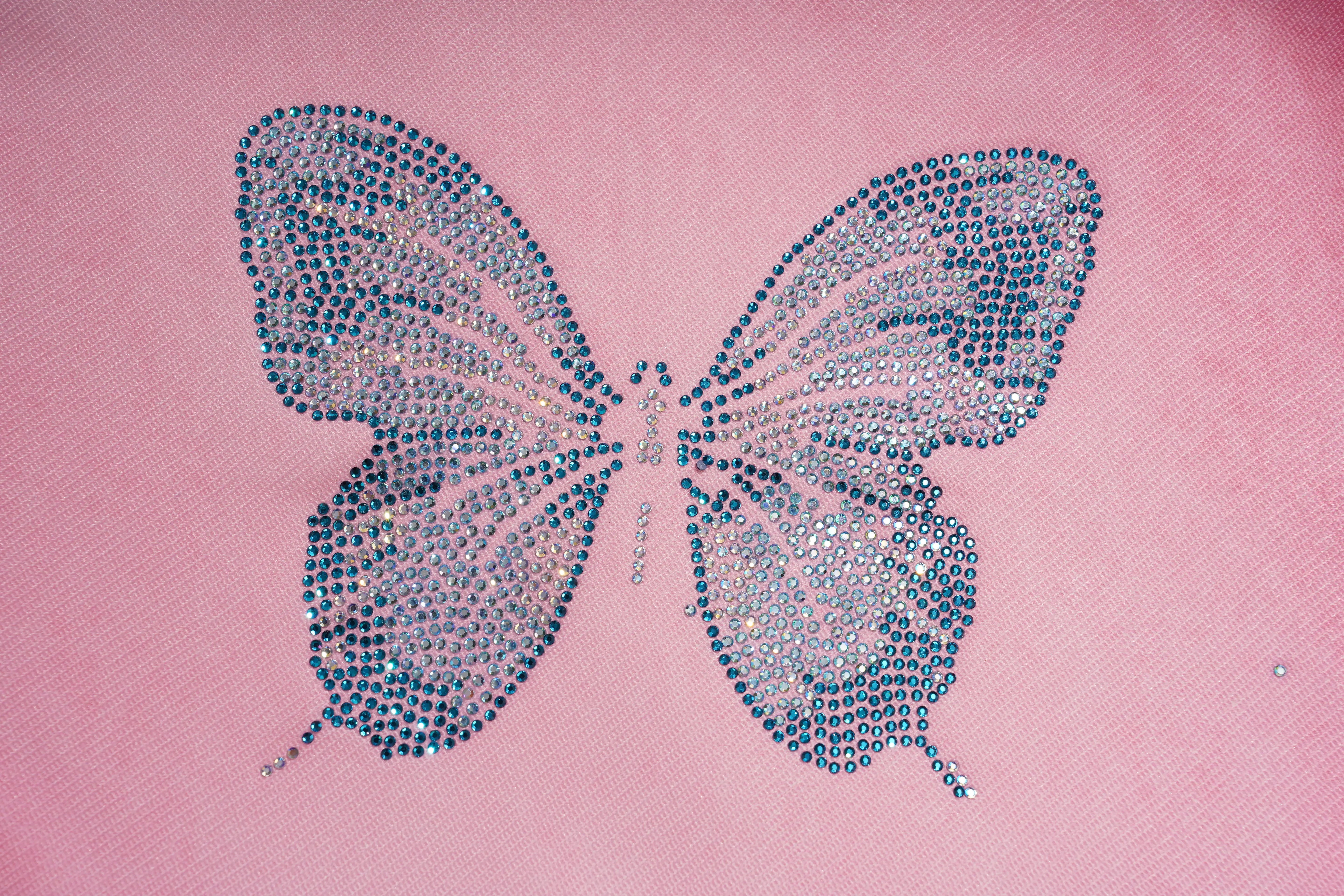 A butterfly-shaped rhinestone embellishment with blue and silver crystals on a pink fabric background. TCH Pink Butterfly Rhinestone Star Wide Leg Jeans