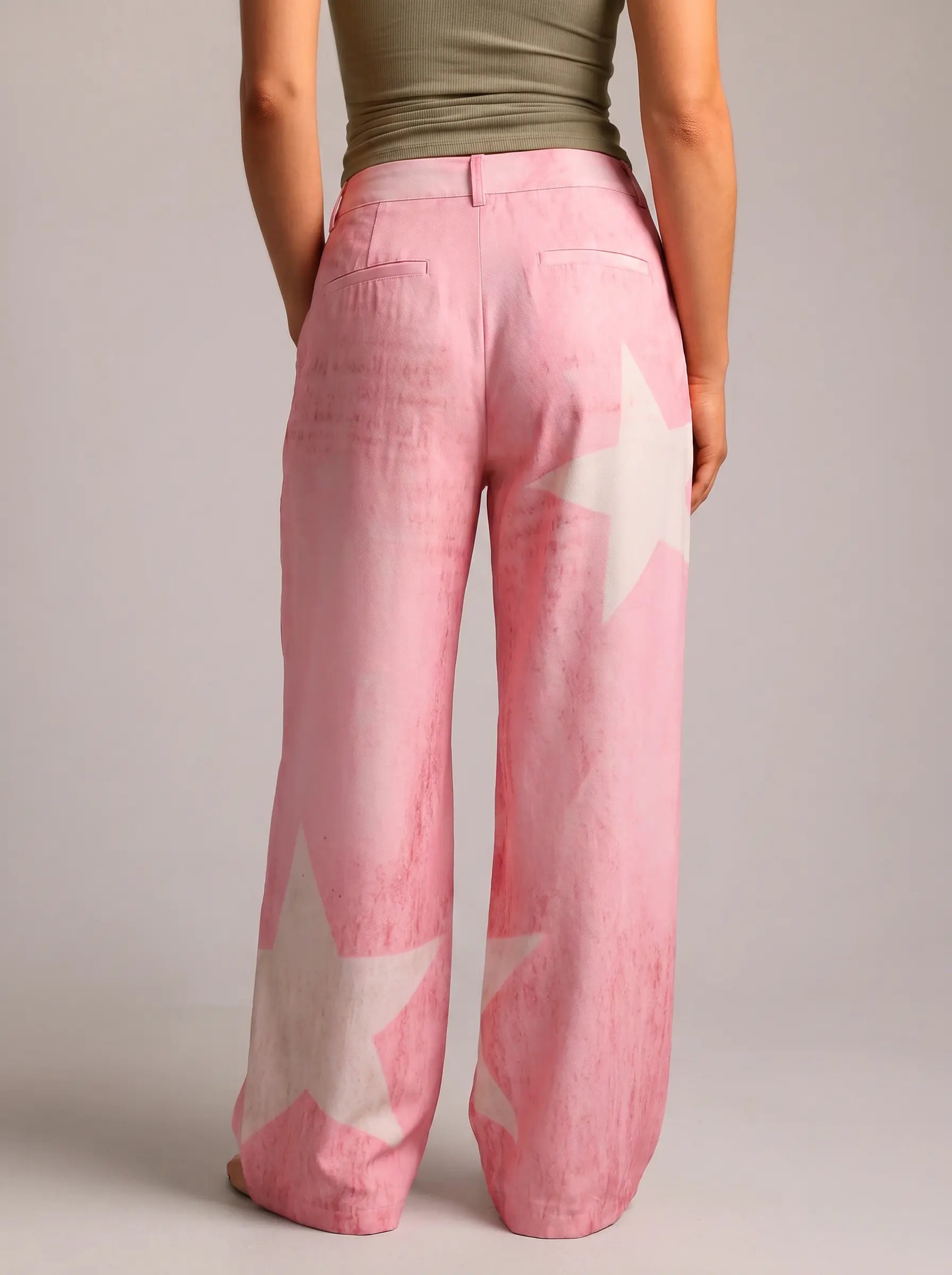 A person shown from the back wearing wide-leg pink pants with large white star prints, paired with an olive green top, against a plain light gray studio background. TCH Pink Butterfly Rhinestone Star Wide Leg Jeans