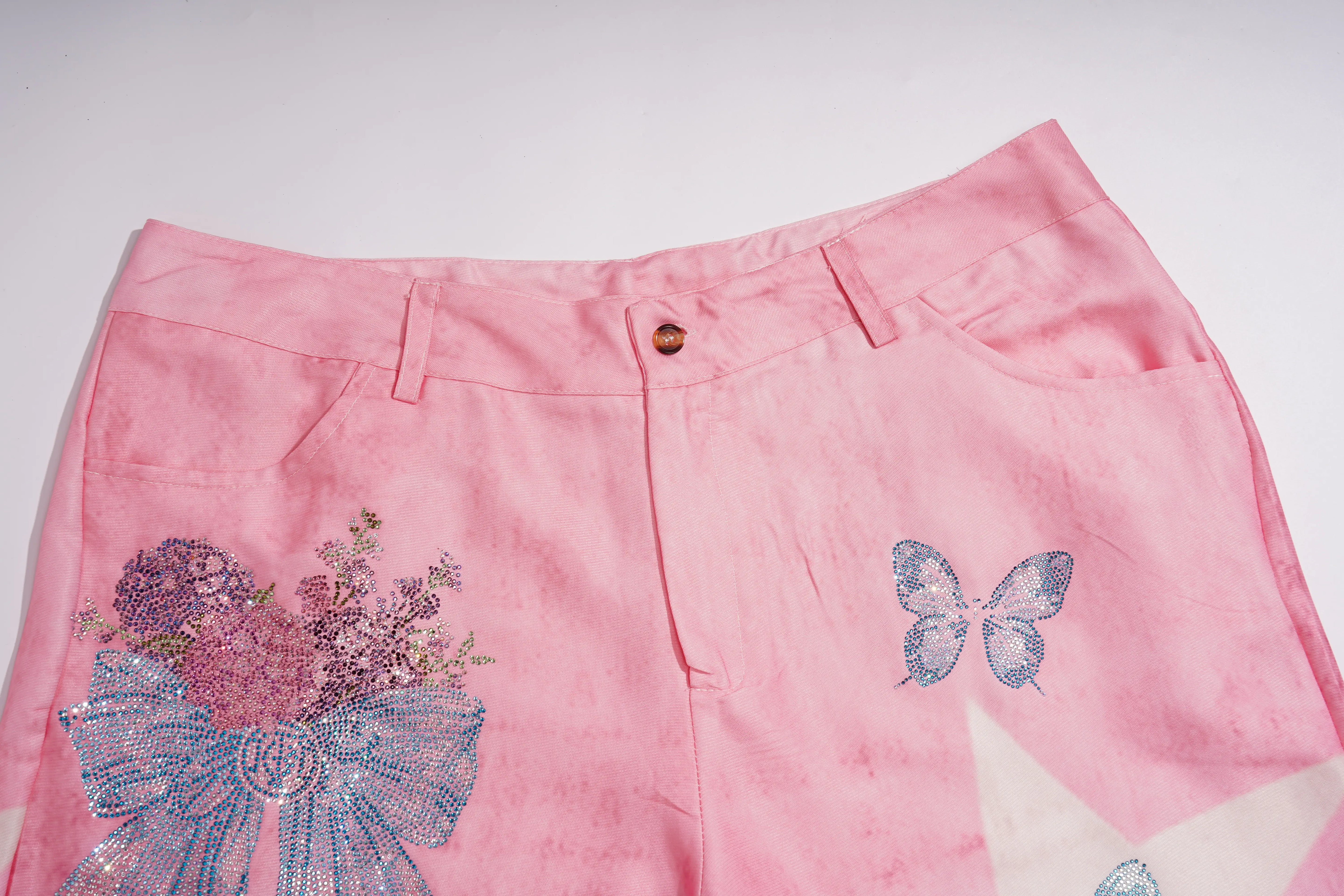 Pink denim shorts featuring a blue butterfly applique on the right thigh and a large blue and purple floral bow design on the left leg, shown against a plain white background. TCH Pink Butterfly Rhinestone Star Wide Leg Jeans