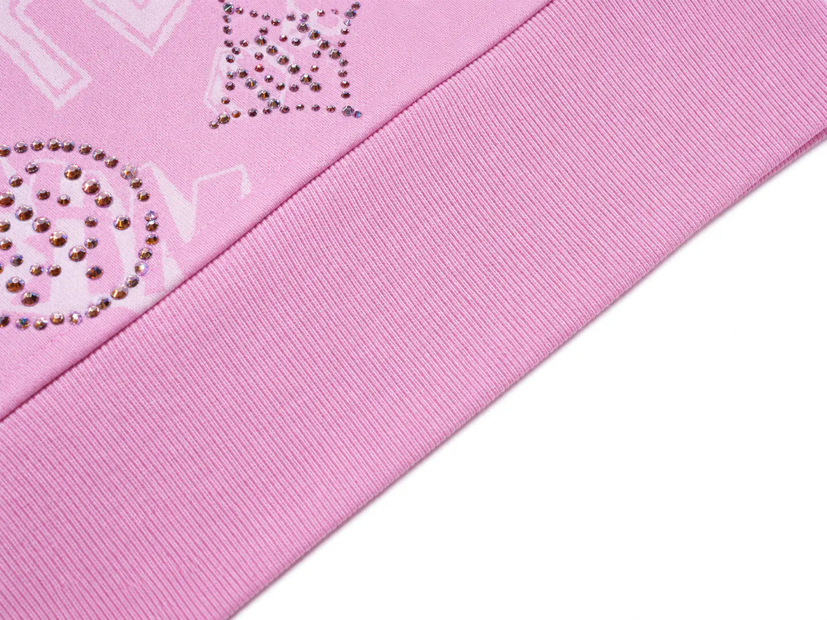 Close-up of a pink ribbed knit fabric with decorative rhinestone embellishments on a matching pink background. TCH Pink Monogram Graphic Zip Up Hoodie