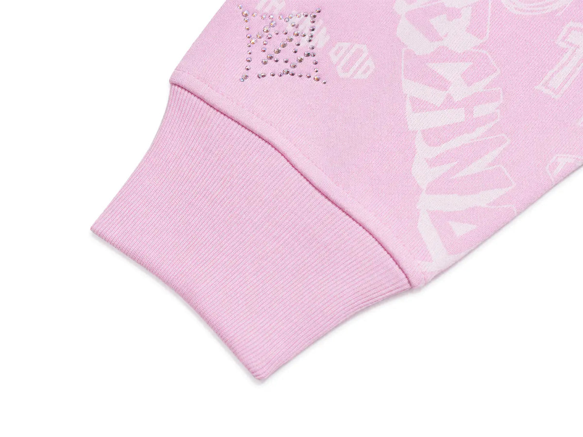 Close-up of a light pink ribbed cuff with a small rhinestone LV logo and a white tonal LV monogram on the fabric, shown on a white background. TCH Pink Monogram Graphic Zip Up Hoodie