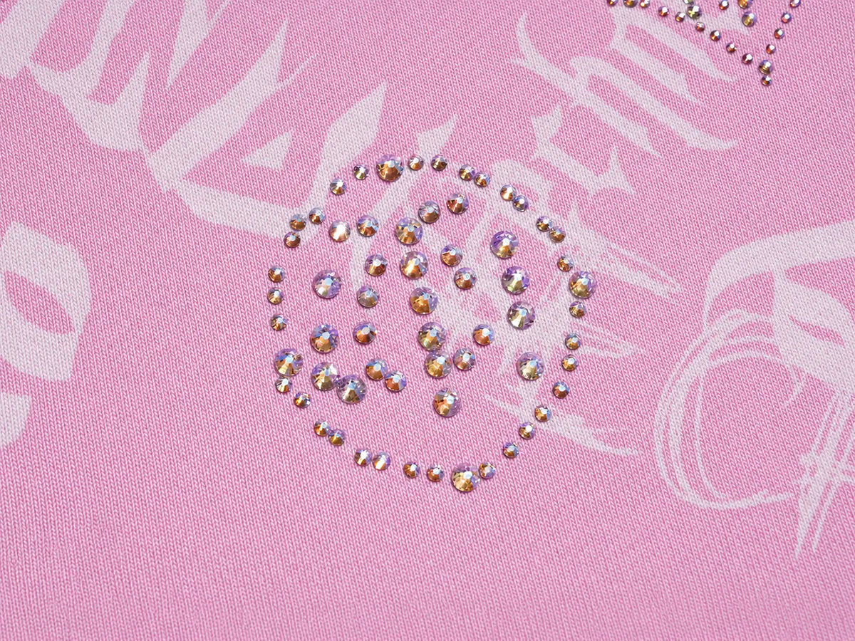 A close-up of a pink fabric surface with a circular arrangement of iridescent rhinestones forming a decorative pattern. TCH Pink Monogram Graphic Zip Up Hoodie