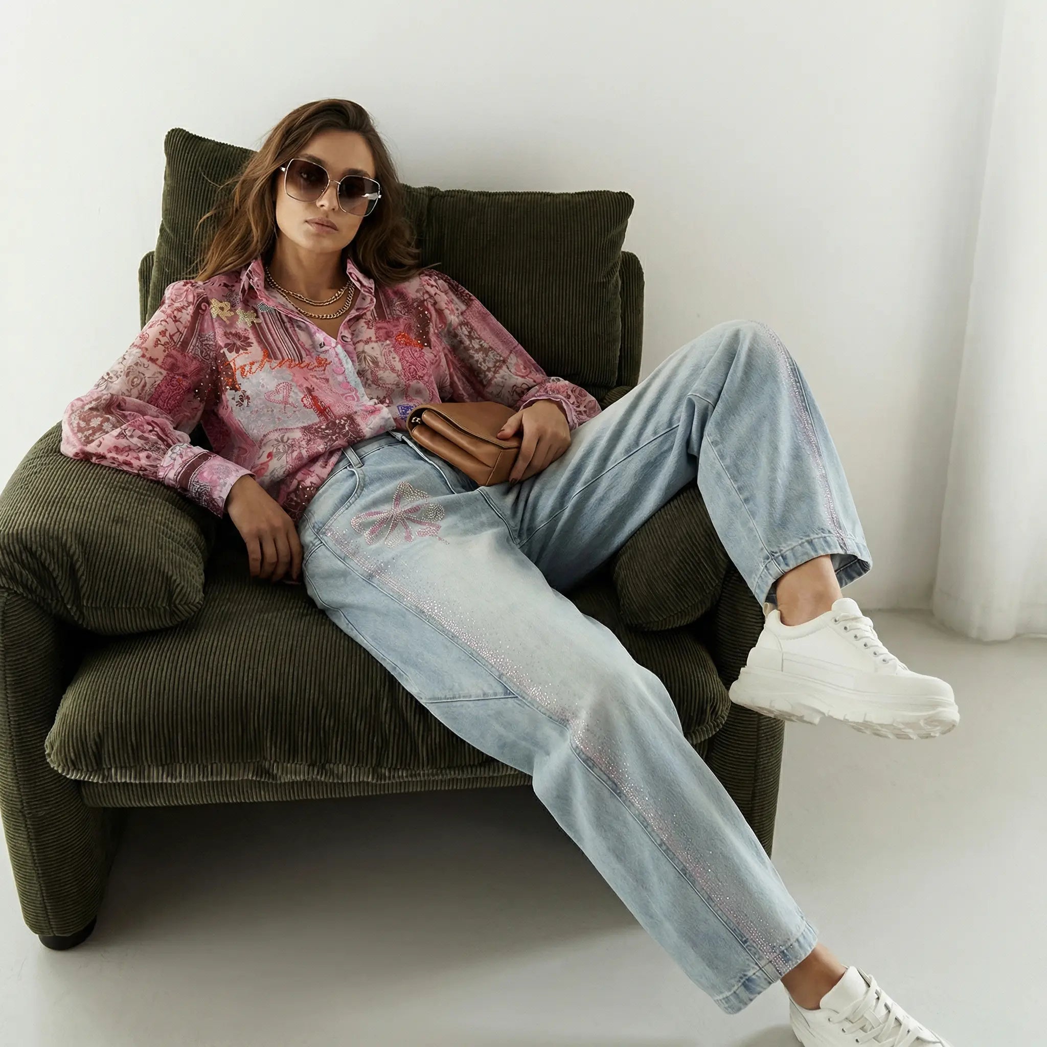 Woman sitting on a brown chair wearing a pink blouse, light blue jeans, and white sneakers. TCH Pink Patchwork Rhinestone Floral Shirt