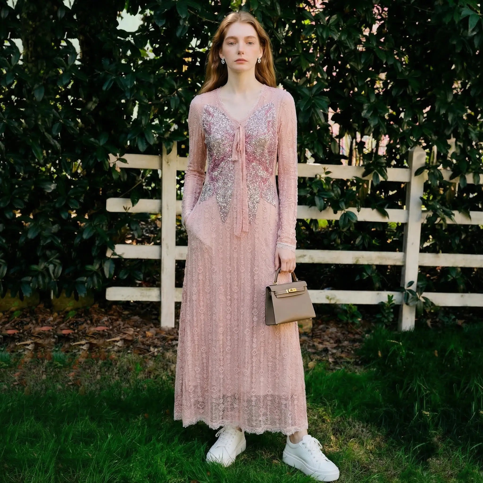 Woman in a long, light pink dress standing outdoors with greenery and a white fence in the background. TCH Pink Rhinestone Bow Lace Layered Dress