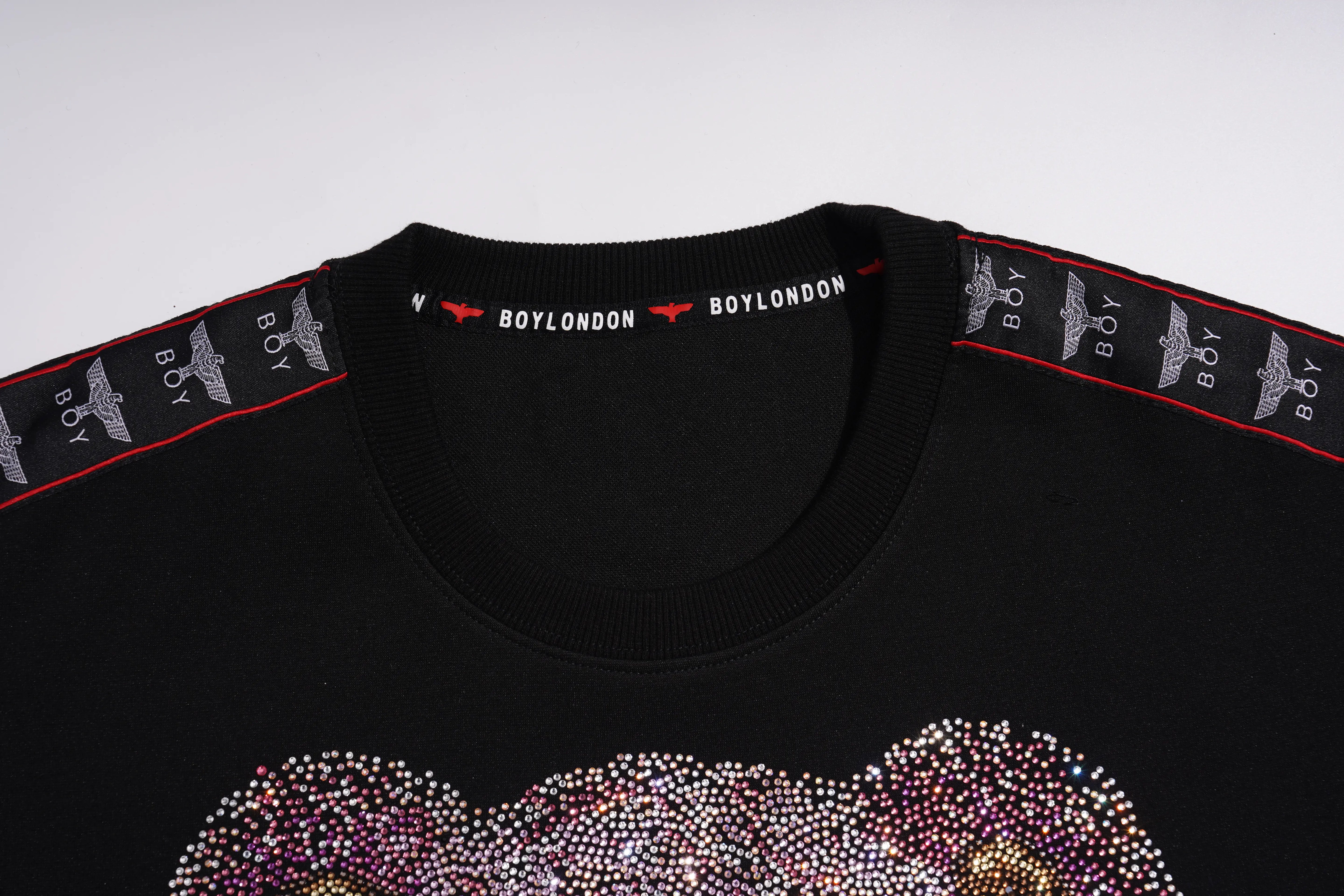 Close-up of a black Boy London crewneck sweatshirt featuring a rhinestone-embellished graphic across the chest and branded tape along the shoulders. TCH Pink Teddy Bear Rhinestone Graphic Black Sweatshirt