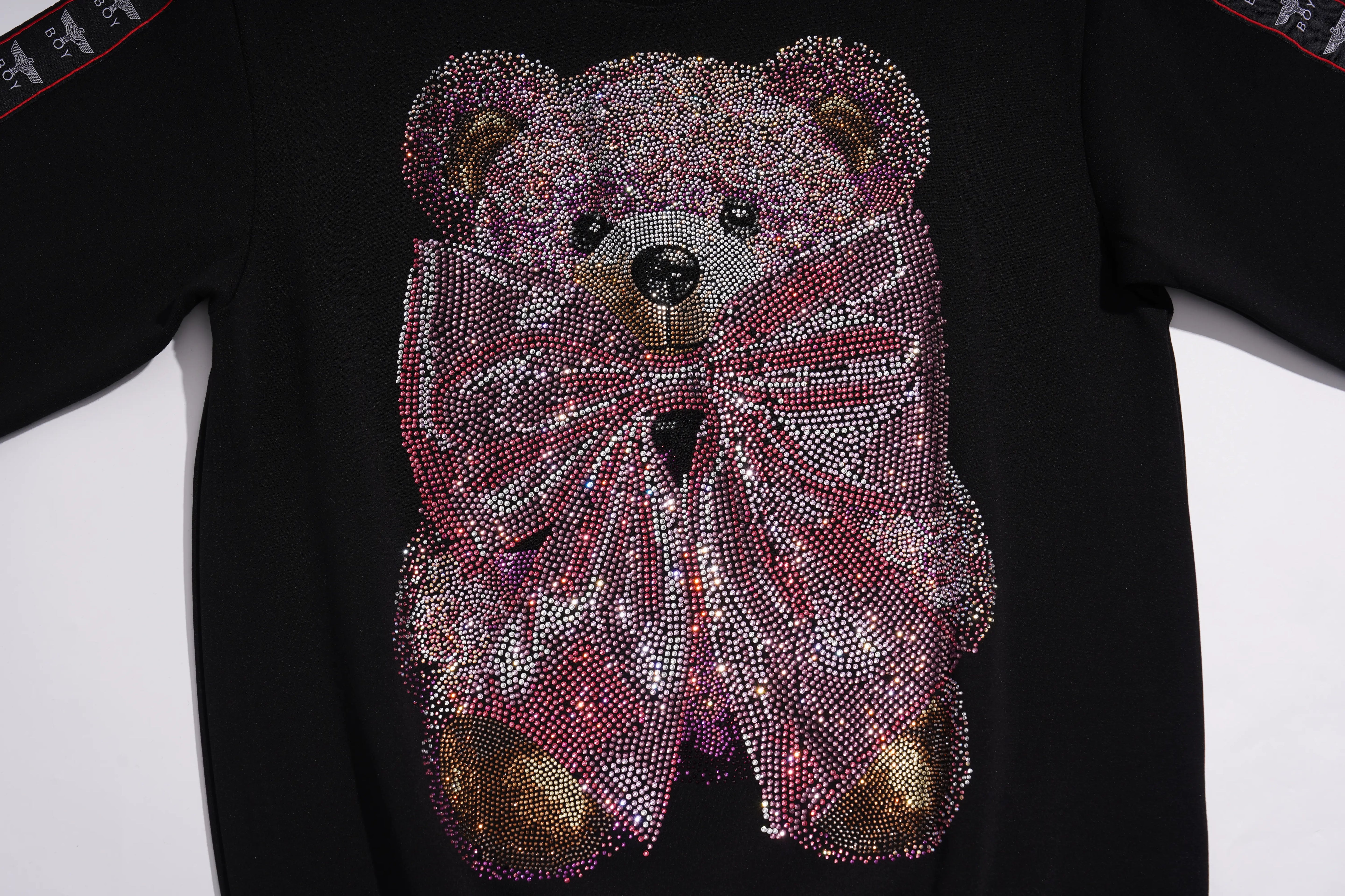 A black short-sleeve T-shirt featuring a large teddy bear face and bow design covered in pink, purple, and silver rhinestones, with small gold-toned accents on the ears and paws. TCH Pink Teddy Bear Rhinestone Graphic Black Sweatshirt