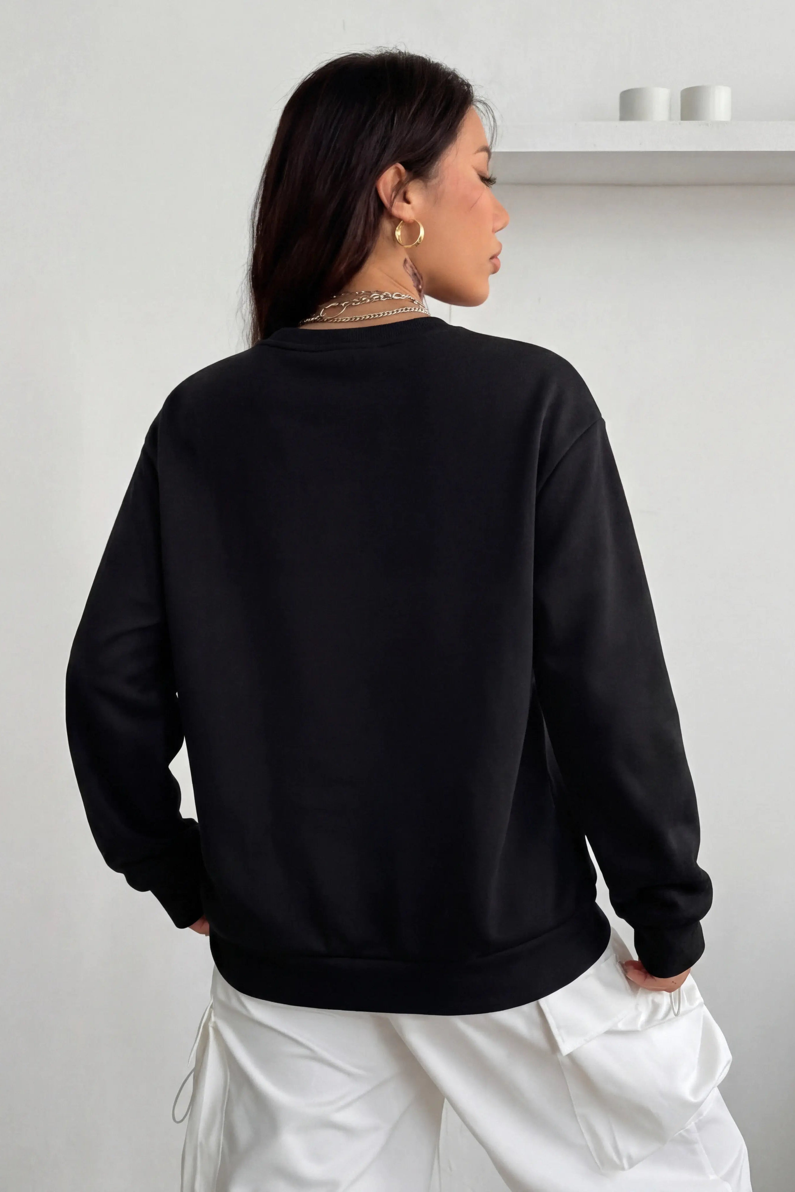 Person wearing a black sweatshirt and white pants against a plain background, TCH Pink Teddy Rhinestone Sweatshirt