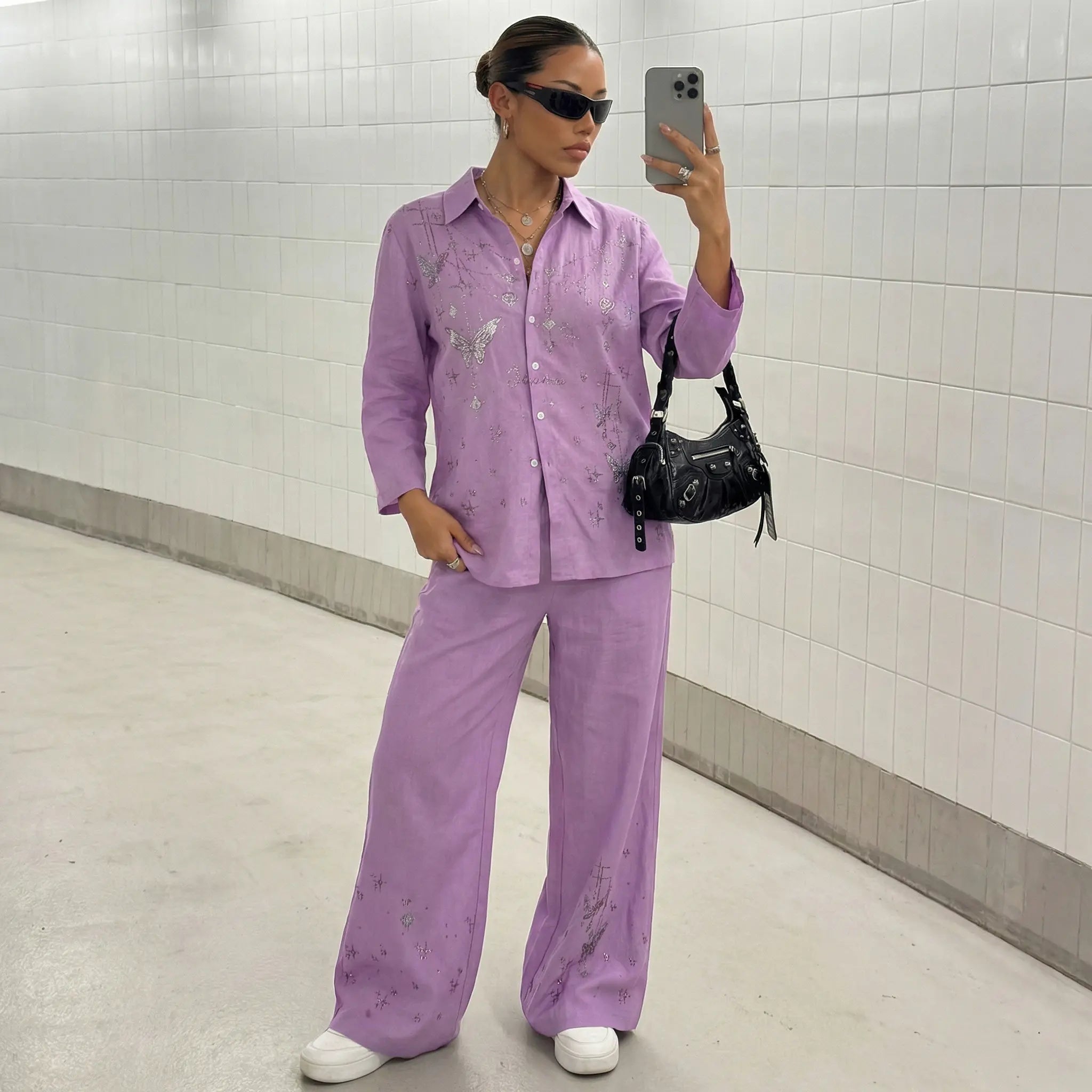Person wearing a matching lavender shirt and pants set, taking a mirror selfie in a tiled hallway. TCH Purple Rhinestone Butterfly Set