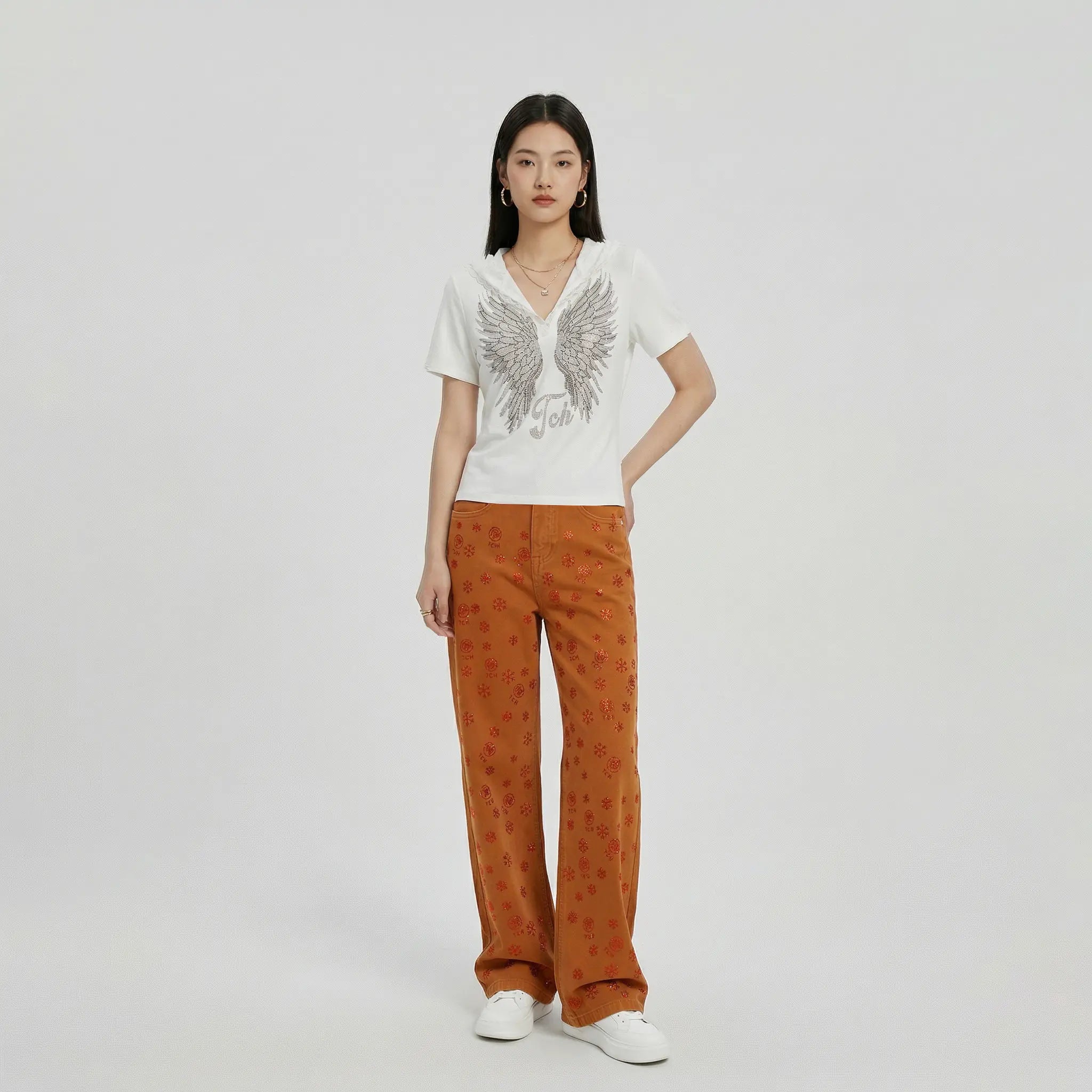 Woman wearing a white top with a graphic design and orange patterned pants on a plain background, TCH Red Snowflake Rhinestone Brown Denim Jeans