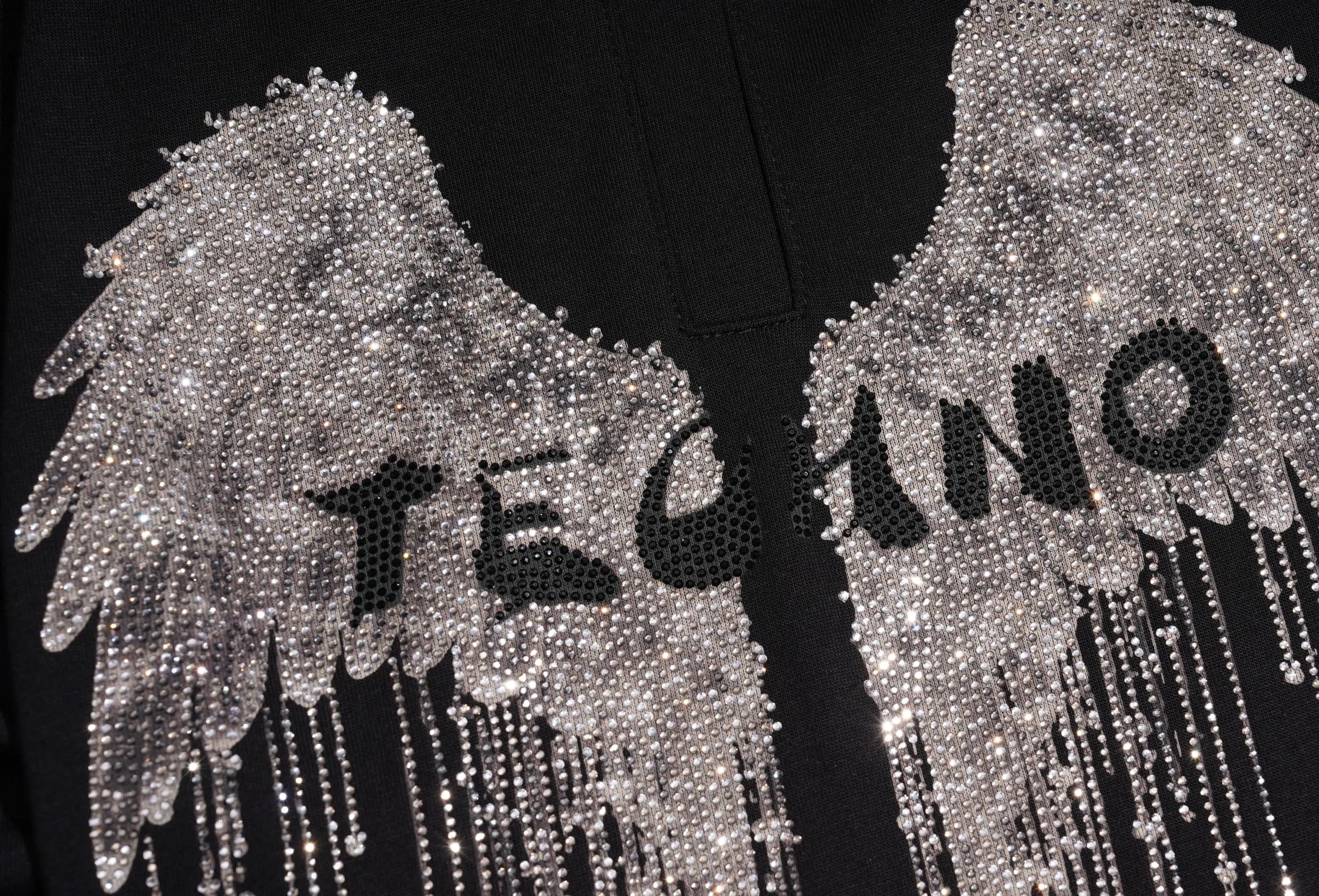 Close-up of a black garment featuring large silver rhinestone angel wings with dangling bead chains and the word 'TECNO' in black rhinestones across the center. TCH Rhinestone Angel Wing Graphic Shorts