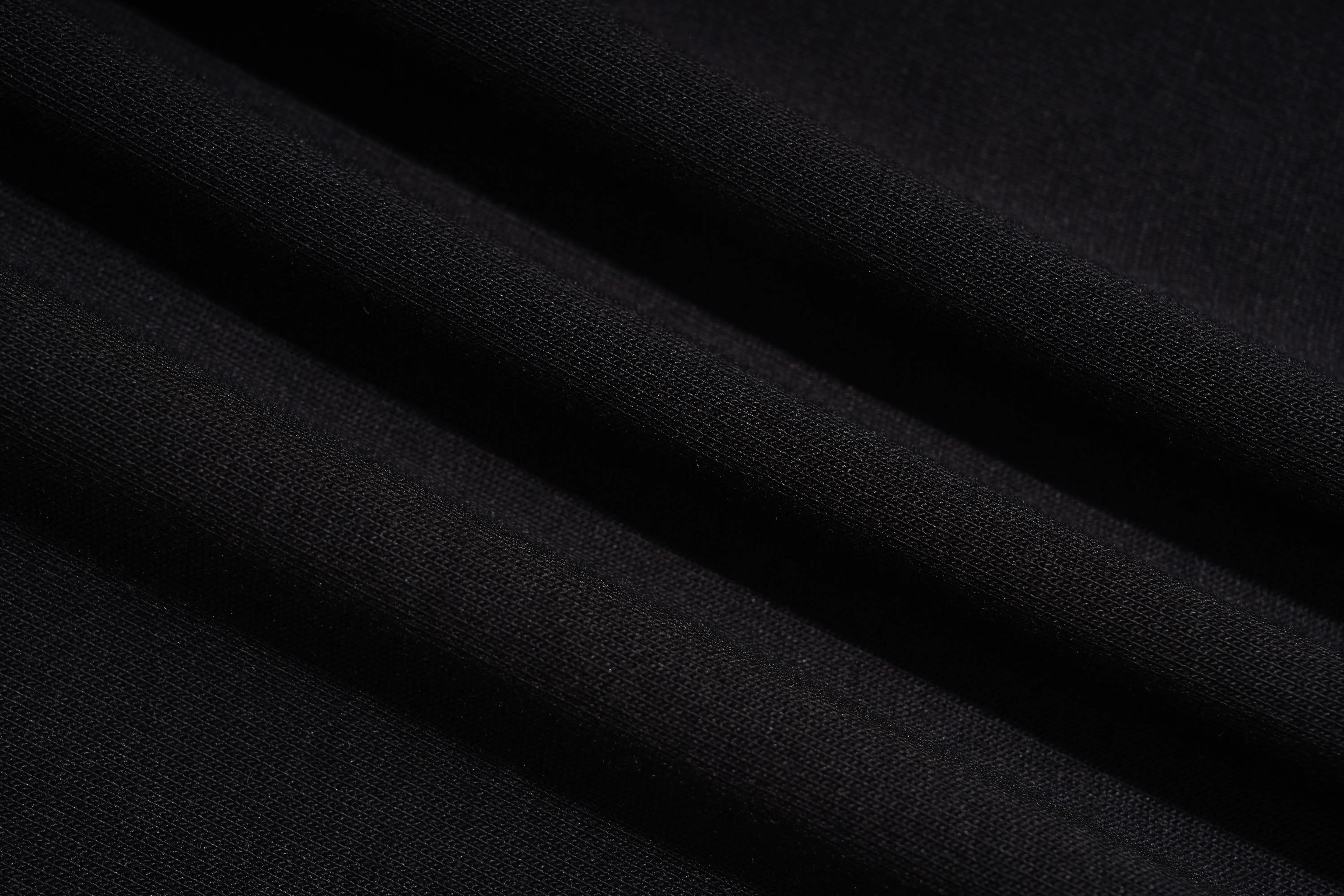 A close-up of draped black fabric with soft diagonal folds showing a fine knit texture. TCH Rhinestone Angel Wing Graphic Shorts