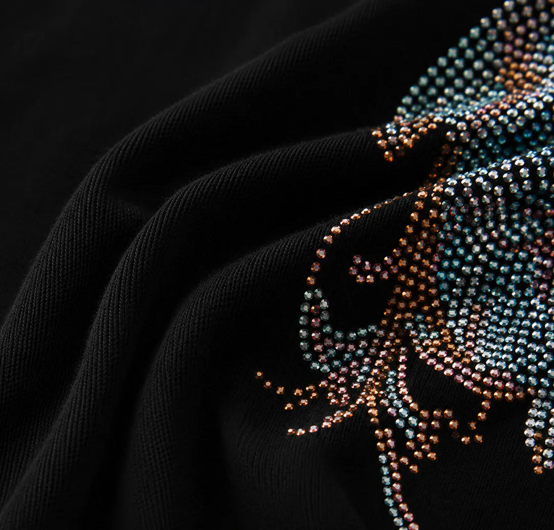 Close-up of a black knit garment featuring an intricate, beaded graphic design in shimmering blue, teal, and copper tones. TCH Rhinestone Angel Wings Graphic T-Shirt