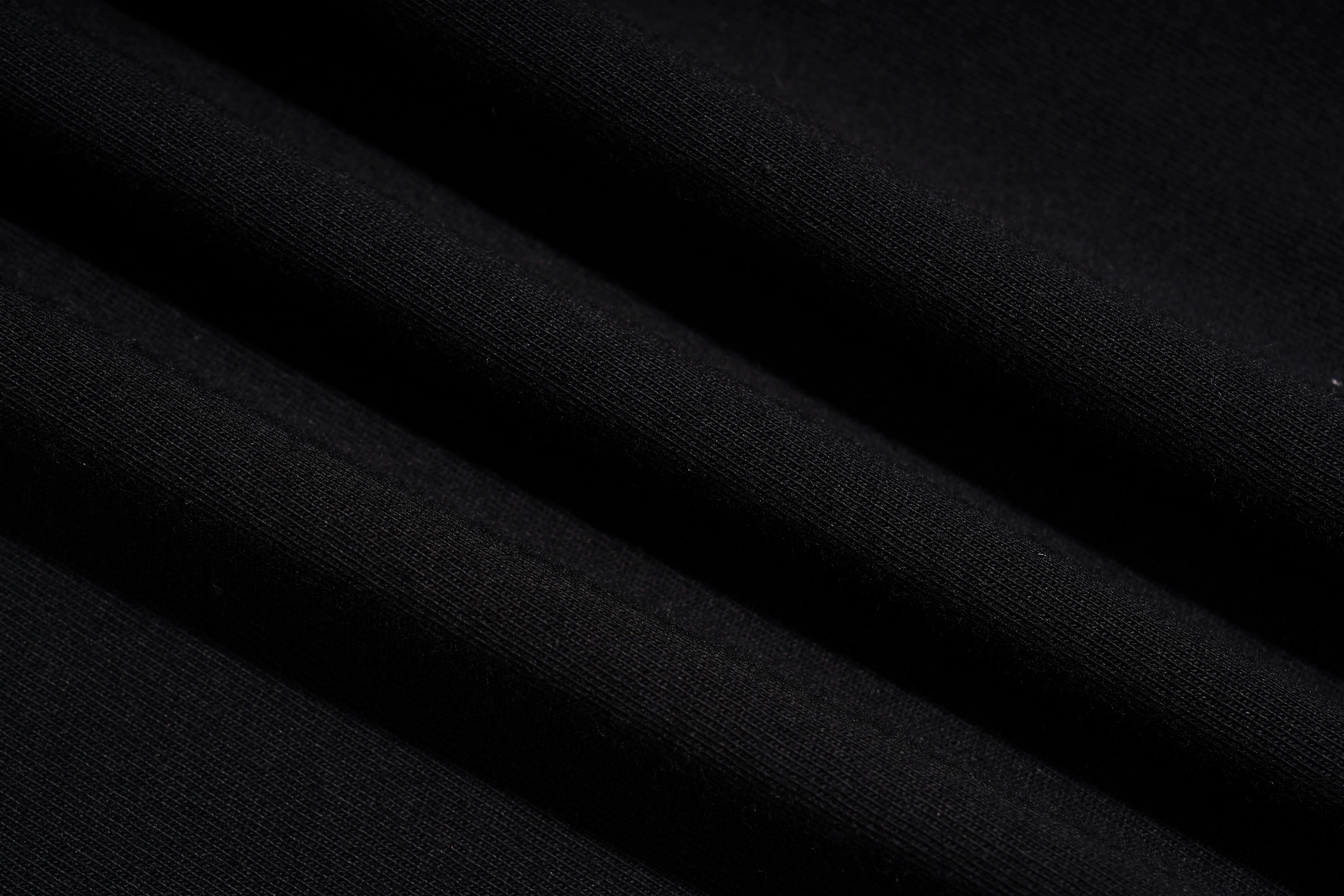 A close-up of draped black fabric with soft diagonal folds showing a fine knit texture. TCH Rhinestone Angel Wings Graphic T-Shirt