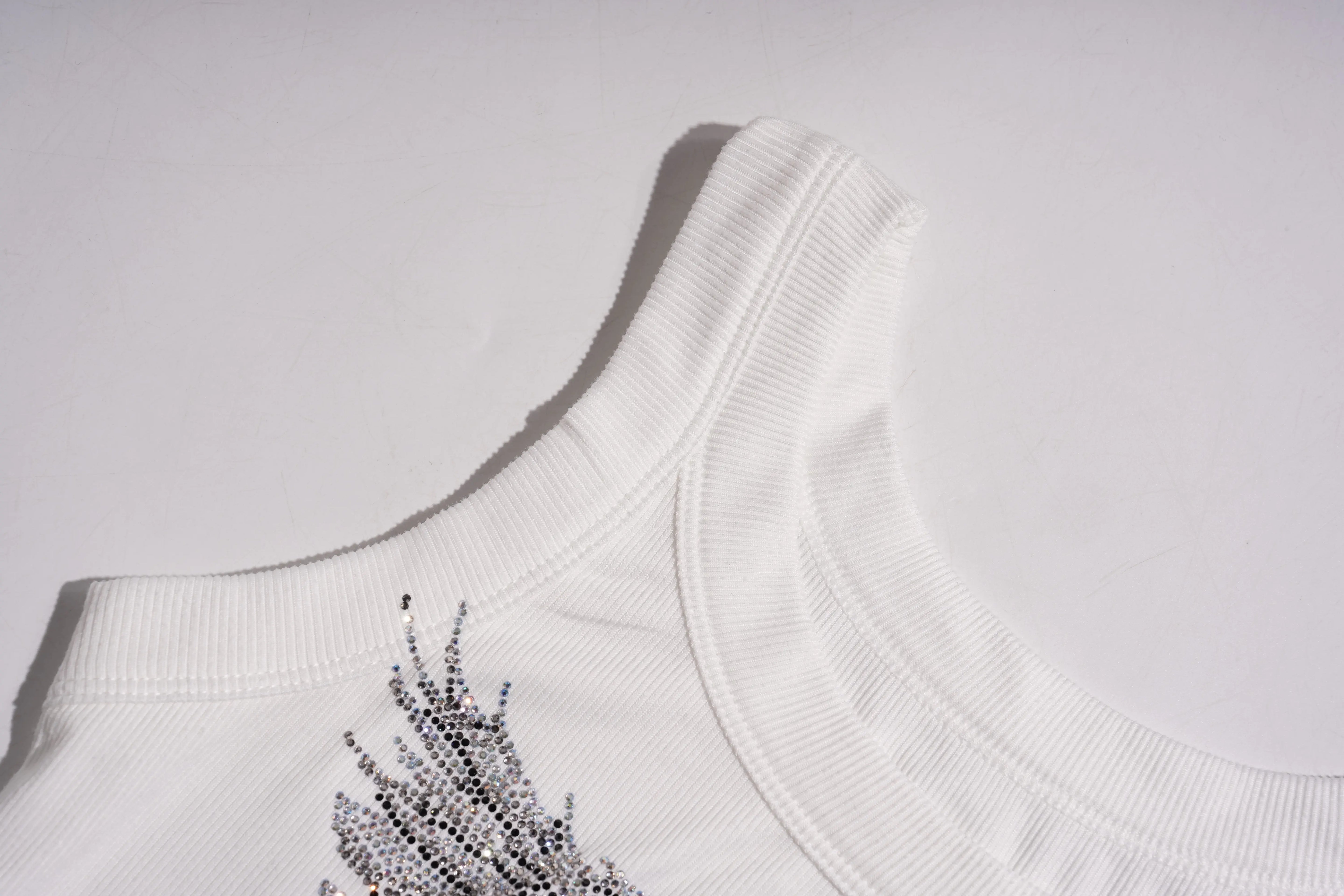 Close-up of a white garment with decorative elements on a light gray background, TCH Rhinestone Angel Wings Ribbed Tank Top