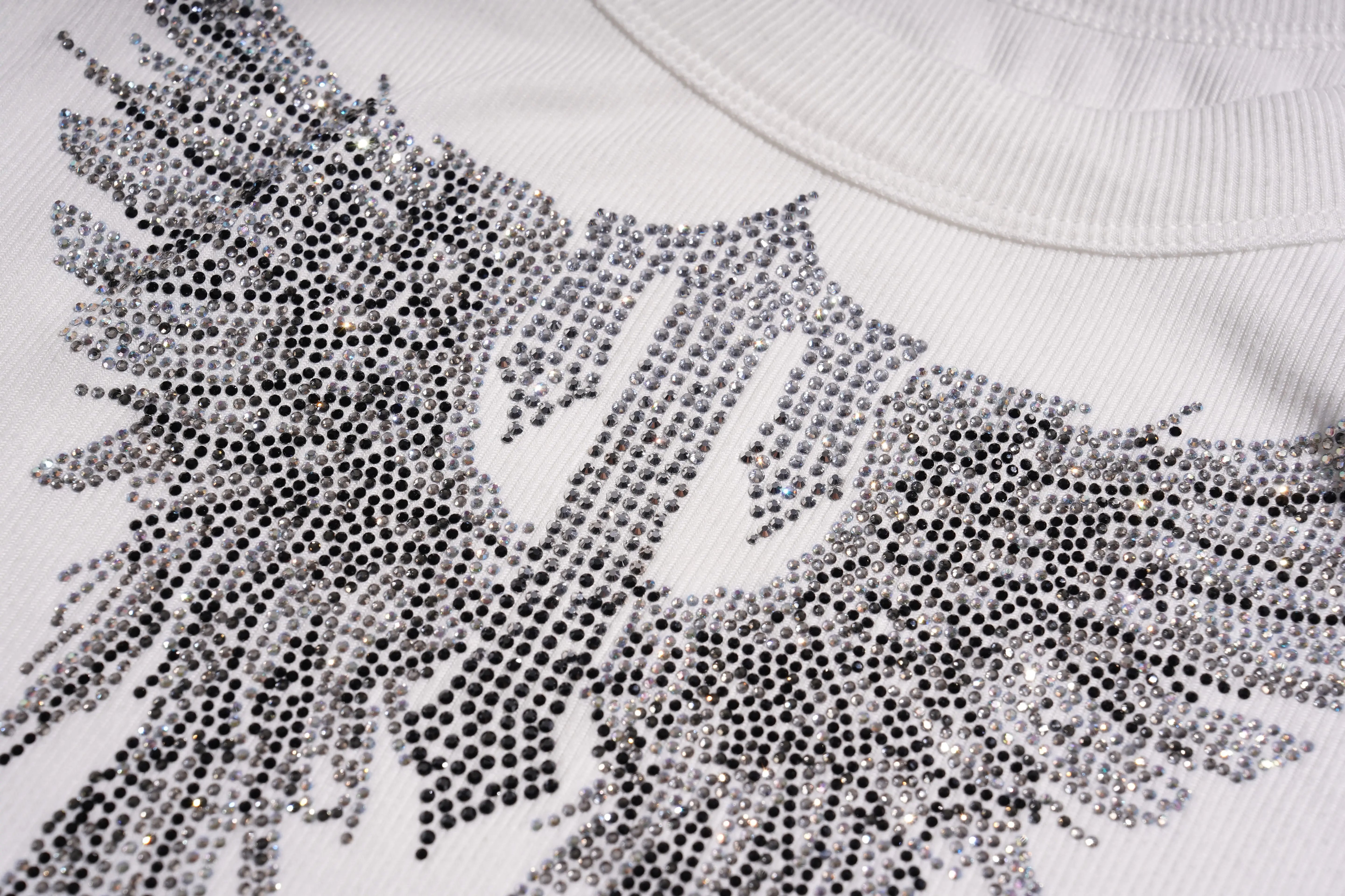 Close-up of a white sweater with a decorative pattern of black and silver rhinestones. TCH Rhinestone Angel Wings Ribbed Tank Top