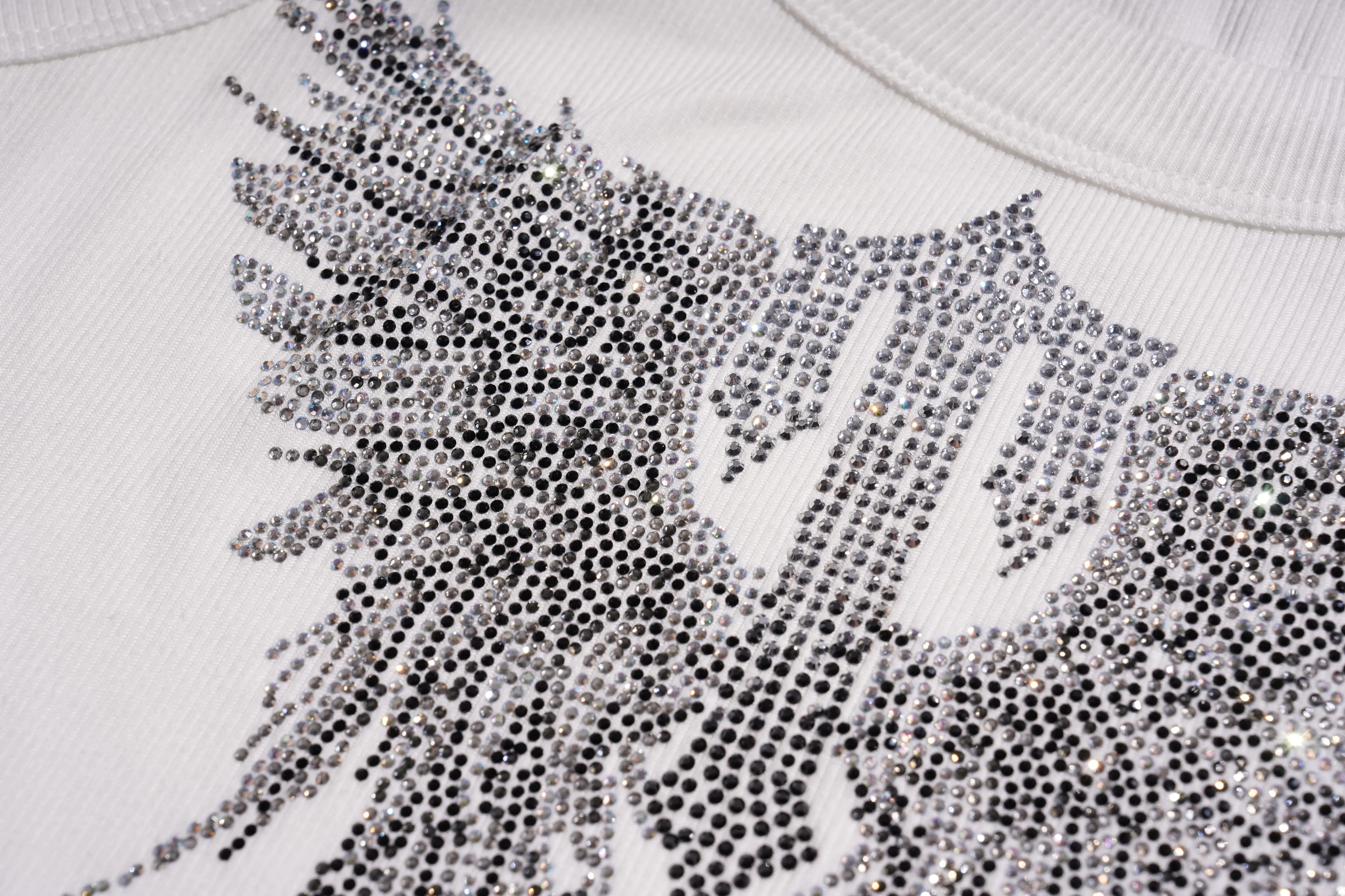 Close-up of a white sweater with a decorative pattern of small black and silver beads. TCH Rhinestone Angel Wings Ribbed Tank Top