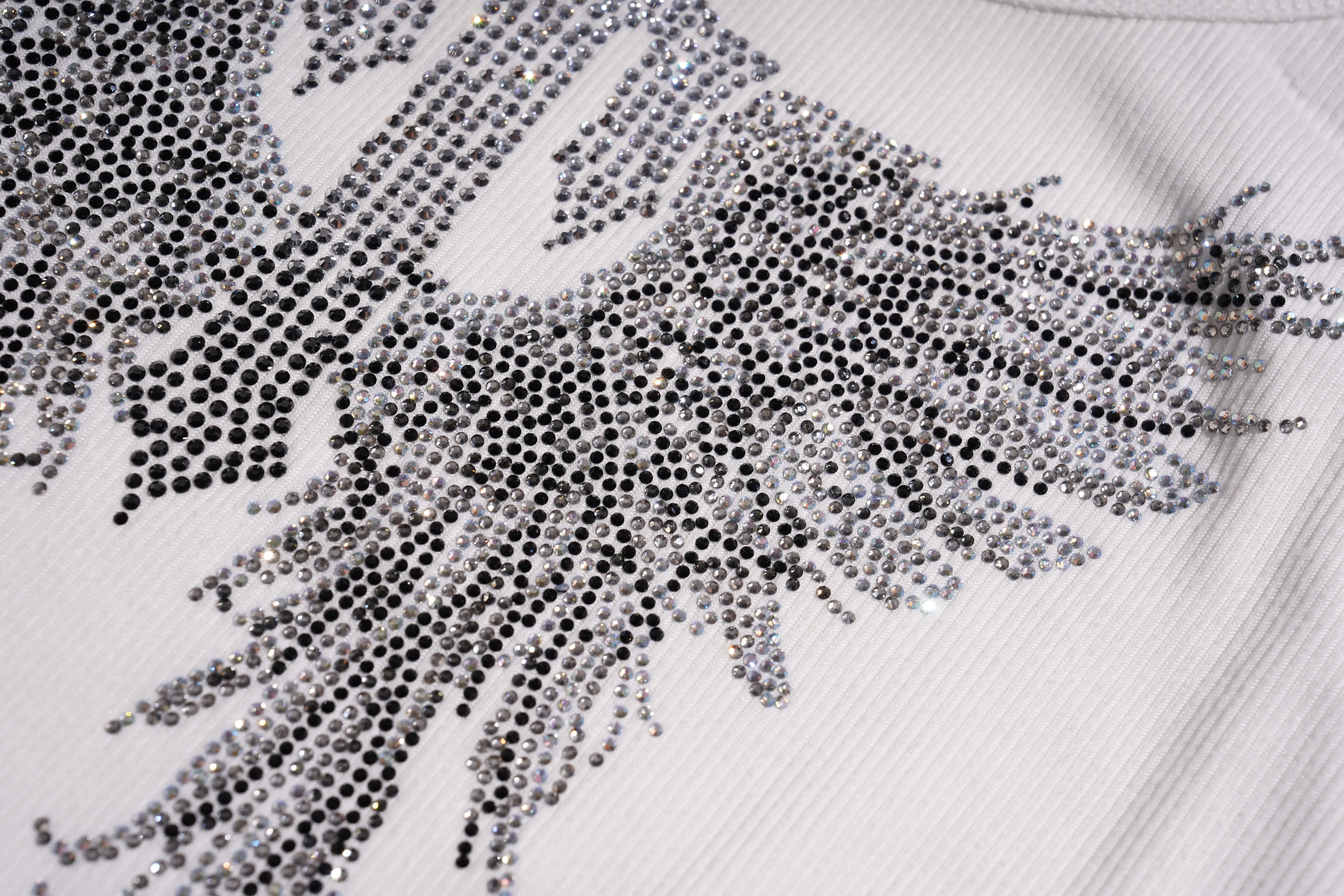 Close-up of a decorative pattern made with small round embellishments on a light fabric background. TCH Rhinestone Angel Wings Ribbed Tank Top