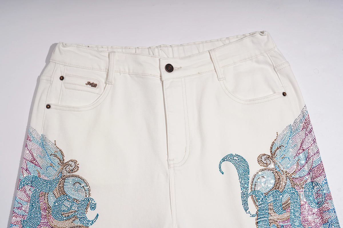 Off-white denim shorts featuring intricate rhinestone and beadwork embroidery in blue, pink, and gold on the lower left and right legs, shown against a plain light background. TCH Rhinestone Angel Wings White Straight-Leg Jeans