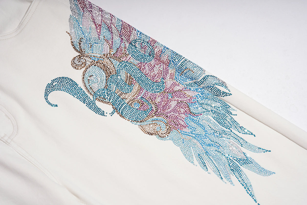 A close-up of a white garment featuring a large, detailed rhinestone wing design in shades of blue, pink, and gold. TCH Rhinestone Angel Wings White Straight-Leg Jeans