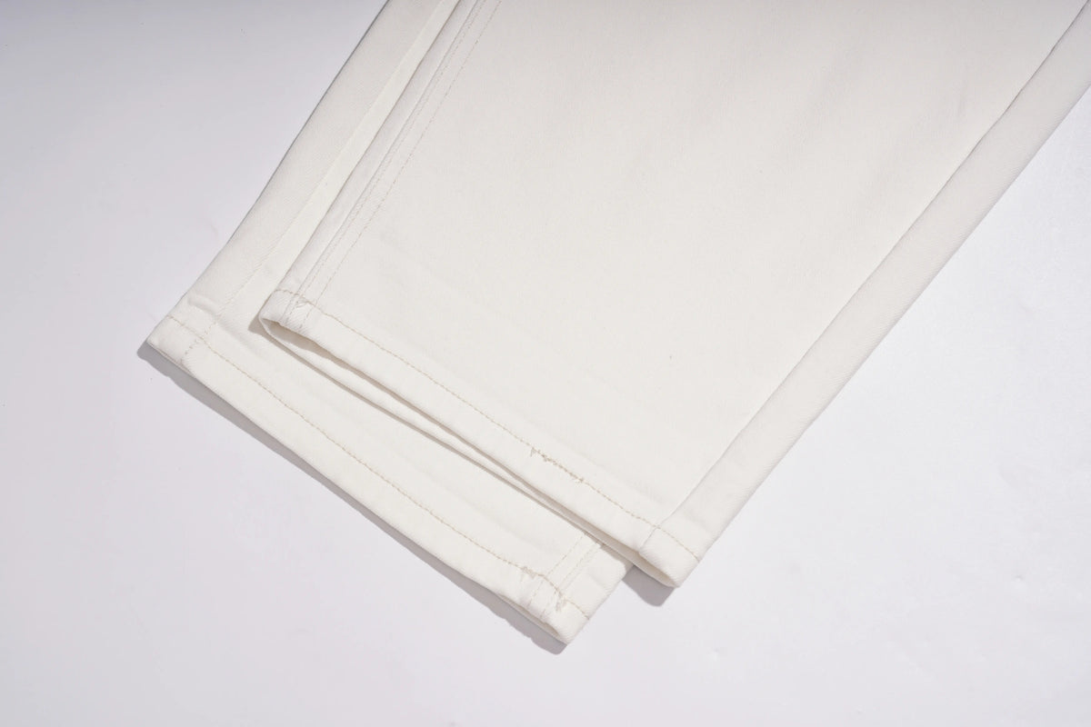A close-up of folded off-white or cream fabric with visible stitching and a slightly textured surface, photographed on a plain light background. TCH Rhinestone Angel Wings White Straight-Leg Jeans