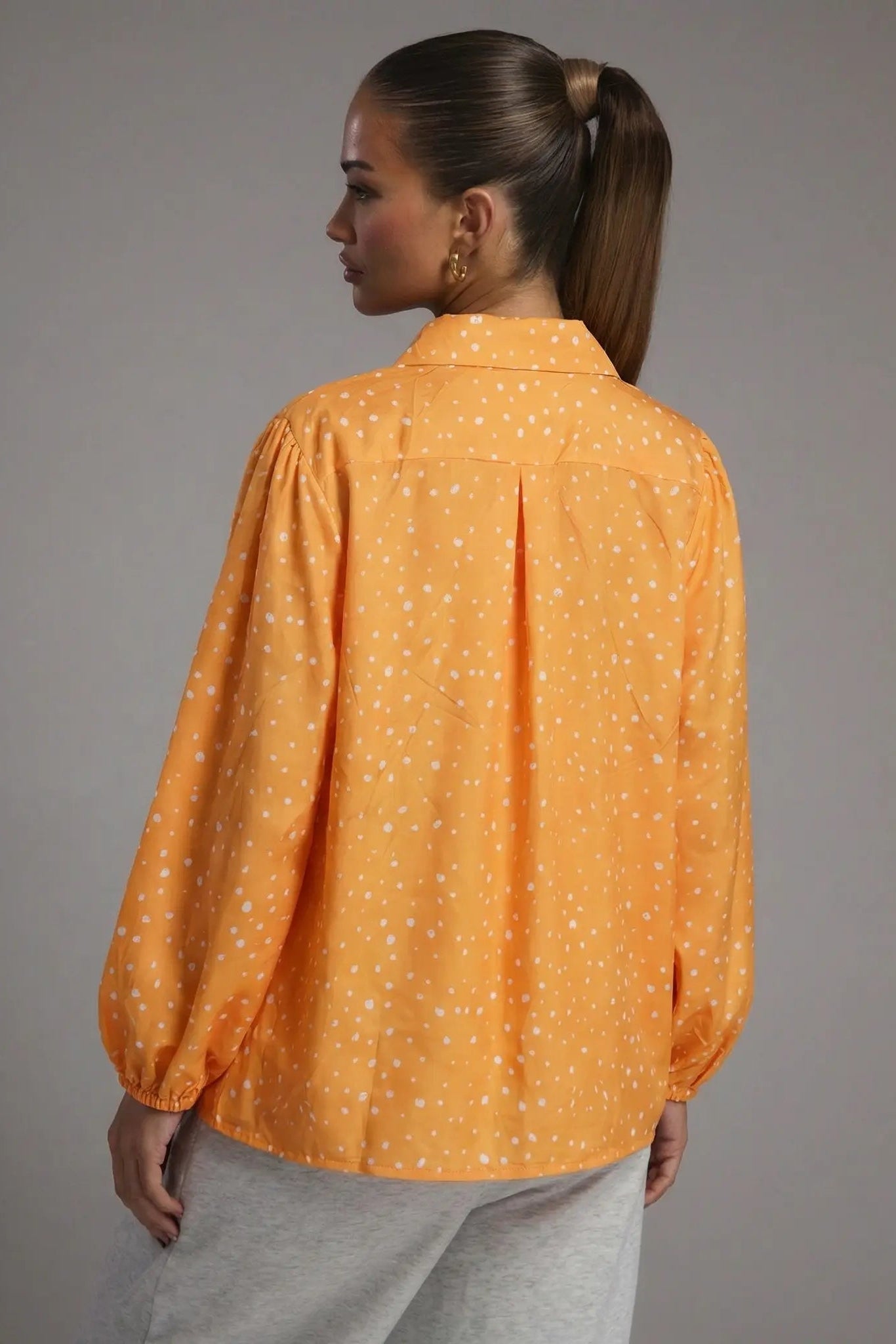 Woman wearing an orange blouse with white polka dots against a gray background, TCH Rhinestone Animal Polka Dot Shirt