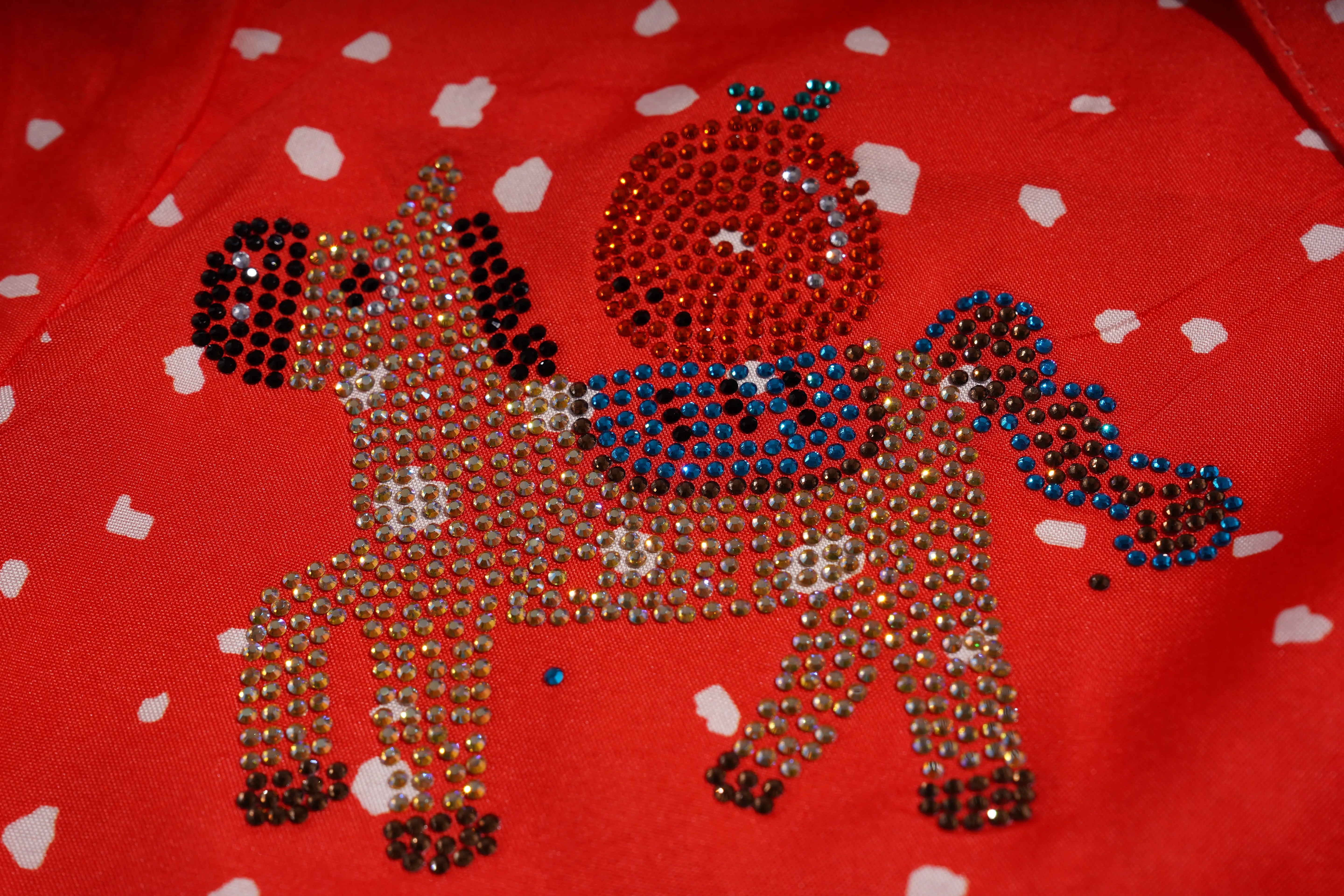 Decorative horse figure made of rhinestones on a red fabric background with white heart patterns. TCH Rhinestone Animal Polka Dot Shirt