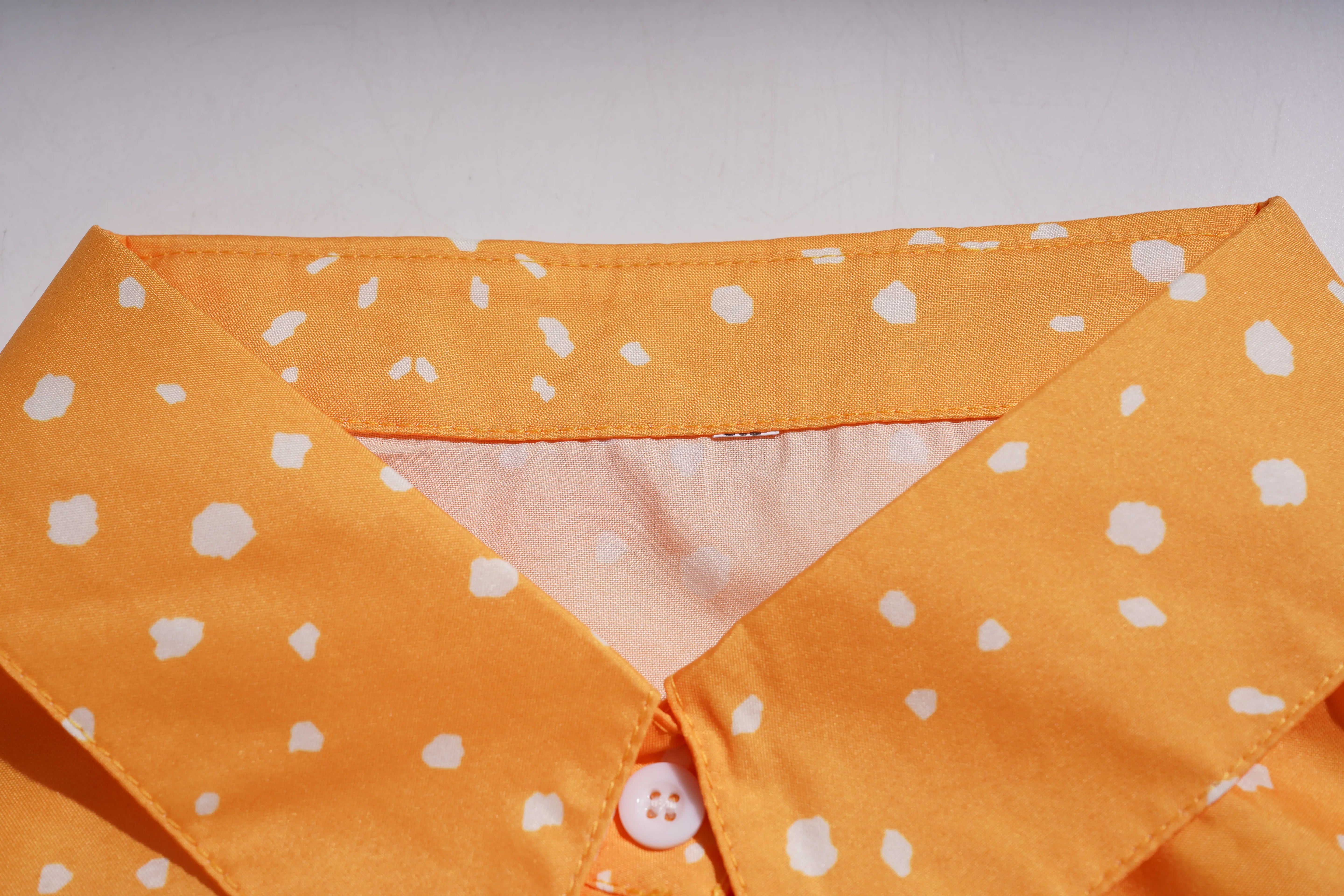 Close-up of an orange shirt with white polka dots on a plain background, TCH Rhinestone Animal Polka Dot Shirt