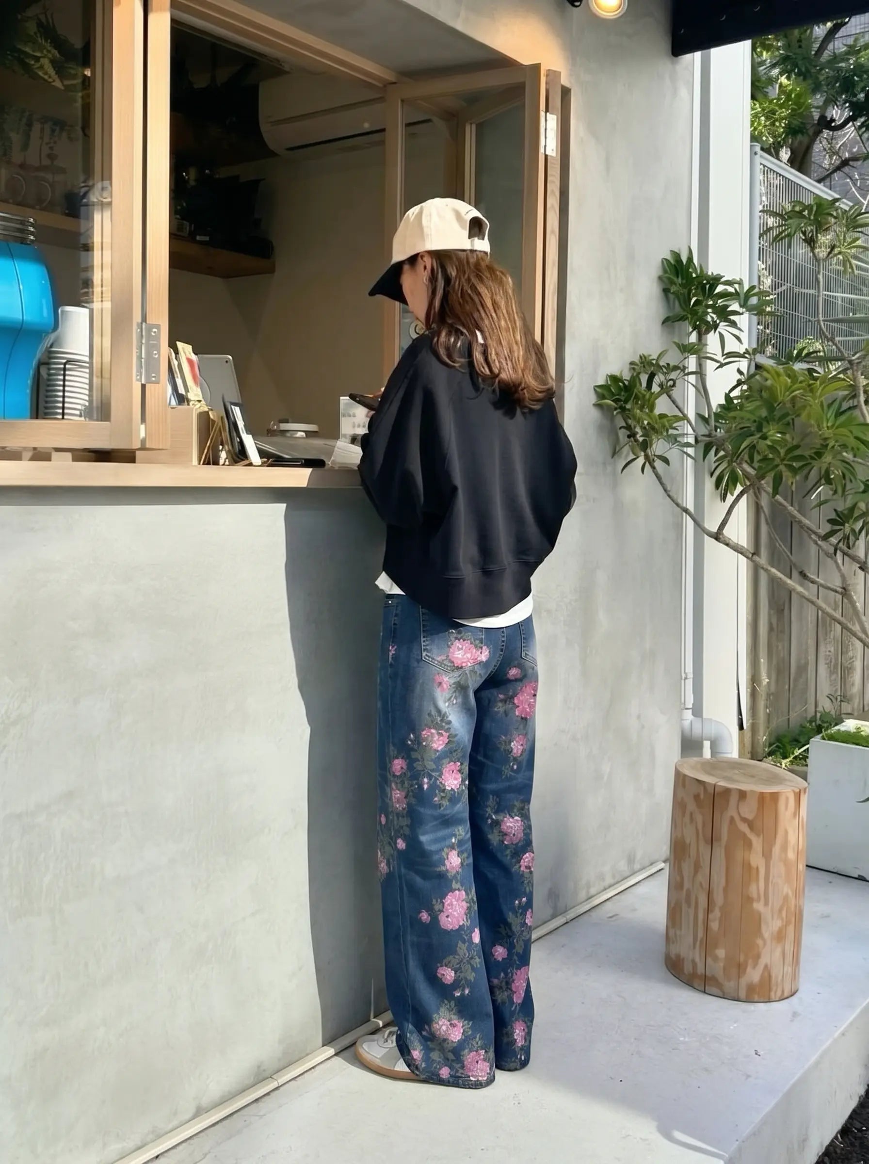 Person wearing a black sweatshirt and floral pants standing outside a small building. TCH Rhinestone Blossom Print Denim Jeans