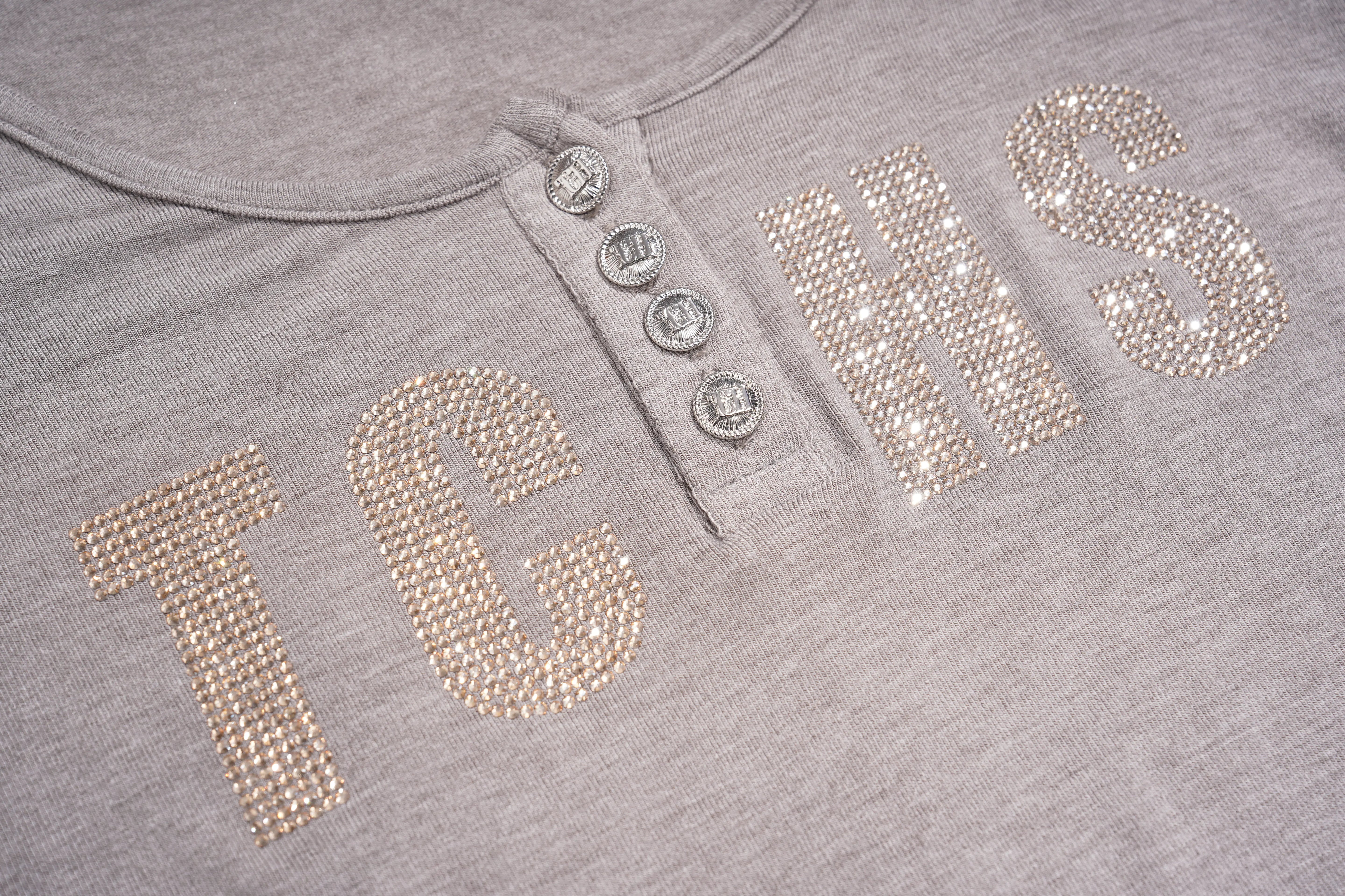 Close-up of a heather gray henley shirt with four silver buttons and large rhinestone-embellished letters spelling 'TCHS' across the chest. TCH Rhinestone Bow 3-Piece Lounge Set