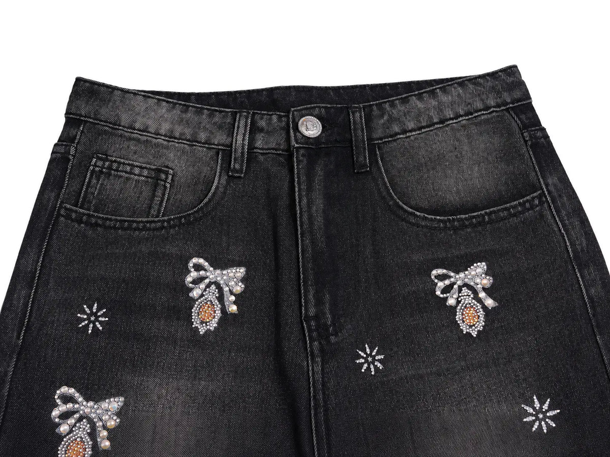 Close-up of black denim jeans featuring decorative embroidered bow motifs with orange centers and silver rhinestone details on the front pockets and upper thighs. TCH Rhinestone Bow & Butterfly Flare Jeans